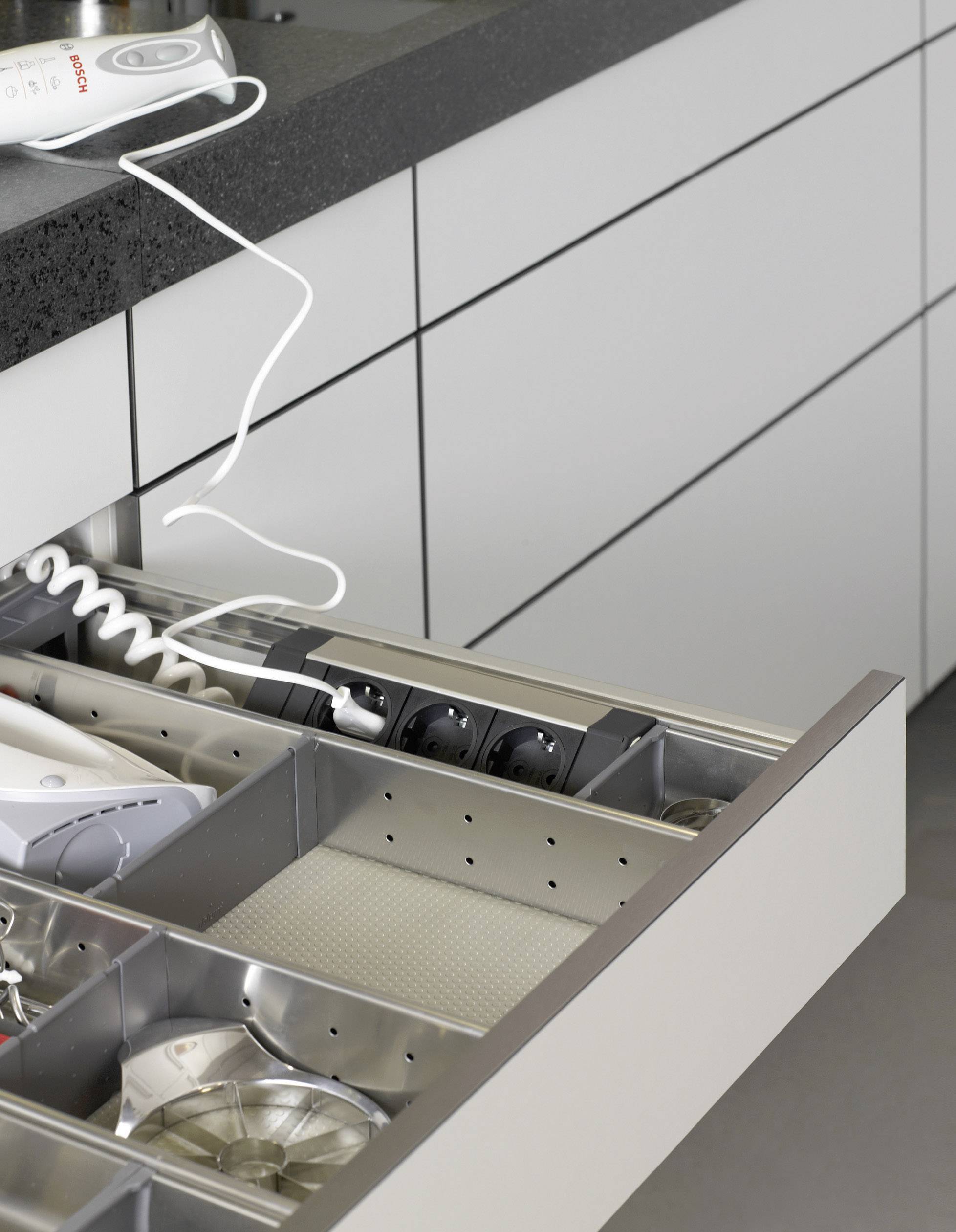 Cassetto della cucina aperto con una multipresa integrata e diversi scomparti per utensili da cucina.