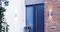 Una moderna porta d'ingresso di colore blu, circondata da muri in mattoni e pareti bianche. Un vaso con fiori rosa è posizionato a sinistra accanto alla porta.