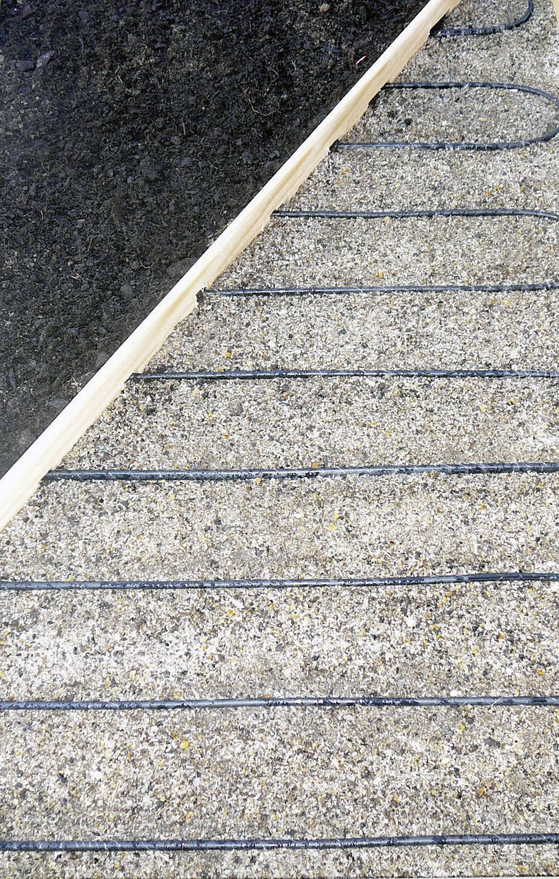 Un pavimento in calcestruzzo con cavo di riscaldamento nero posato a spirale per il riscaldamento a pavimento. Sopra un tappeto, che mostra la struttura del riscaldamento.