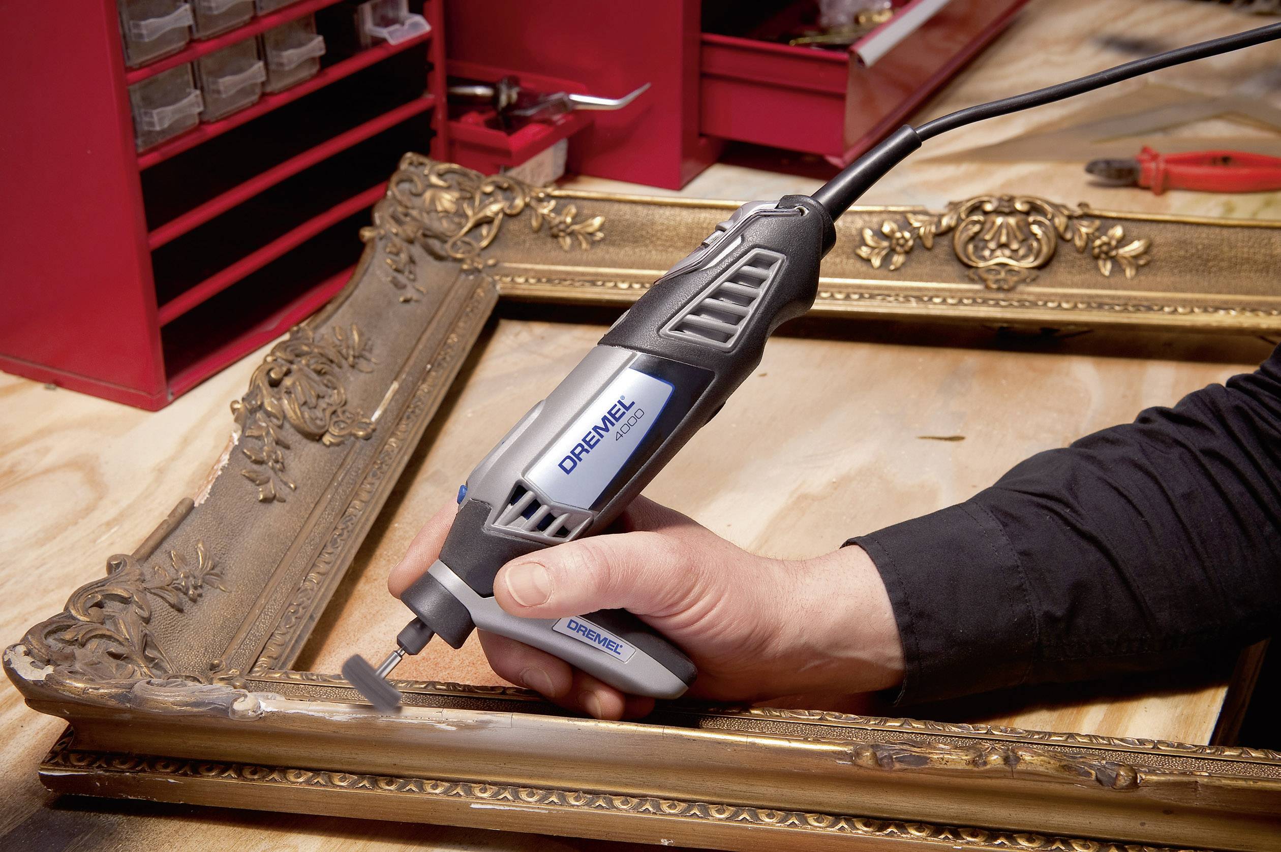 Una persona sta restaurando una cornice dorata e decorata utilizzando un attrezzo manuale in un laboratorio.