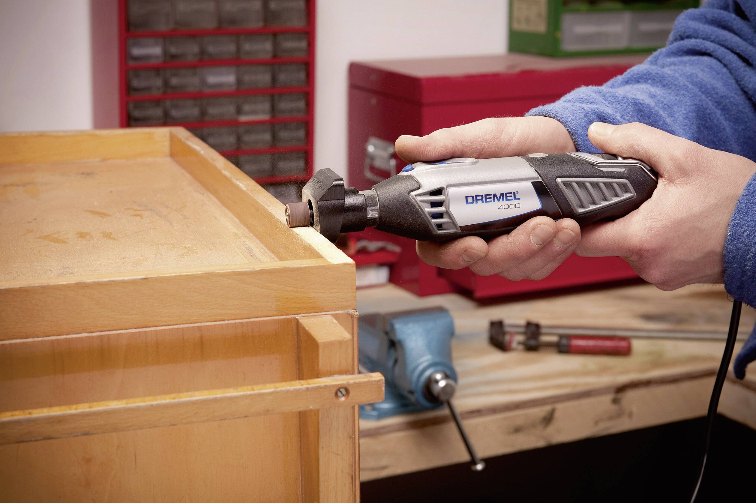 Una persona sta levigando il bordo di un pezzo di legno con uno strumento Dremel, indossando una giacca blu. Banco da lavoro sullo sfondo.