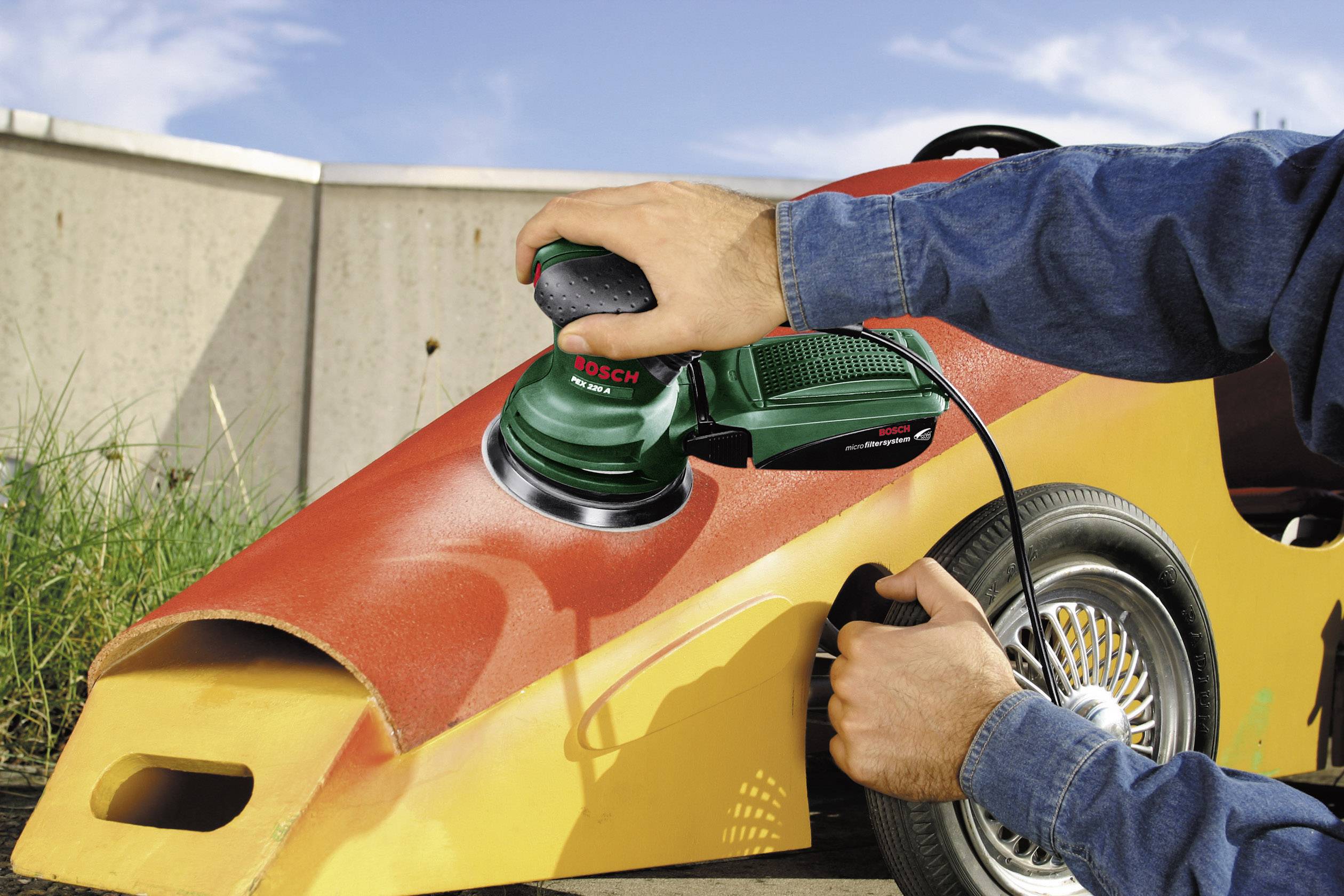 Una persona sta levigando la carrozzeria di un veicolo con un utensile elettrico per la levigatura. Il veicolo ha un design colorato e vivace.