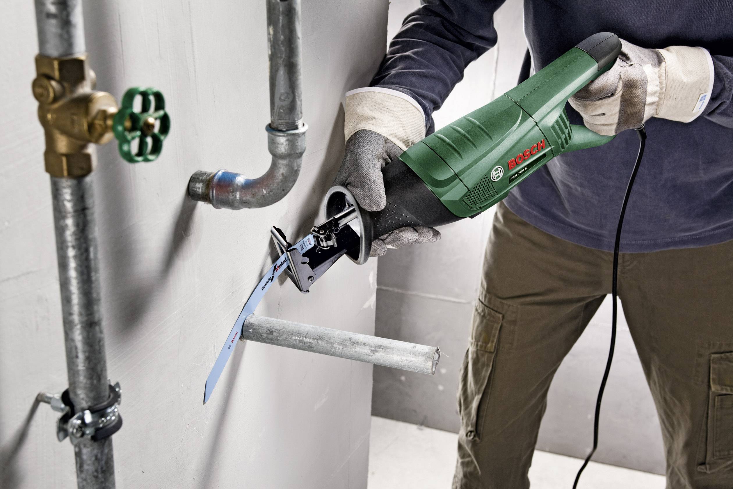 Una persona sta segando un tubo metallico con una sega alternativa Bosch. Indossa guanti protettivi e occhiali di protezione.