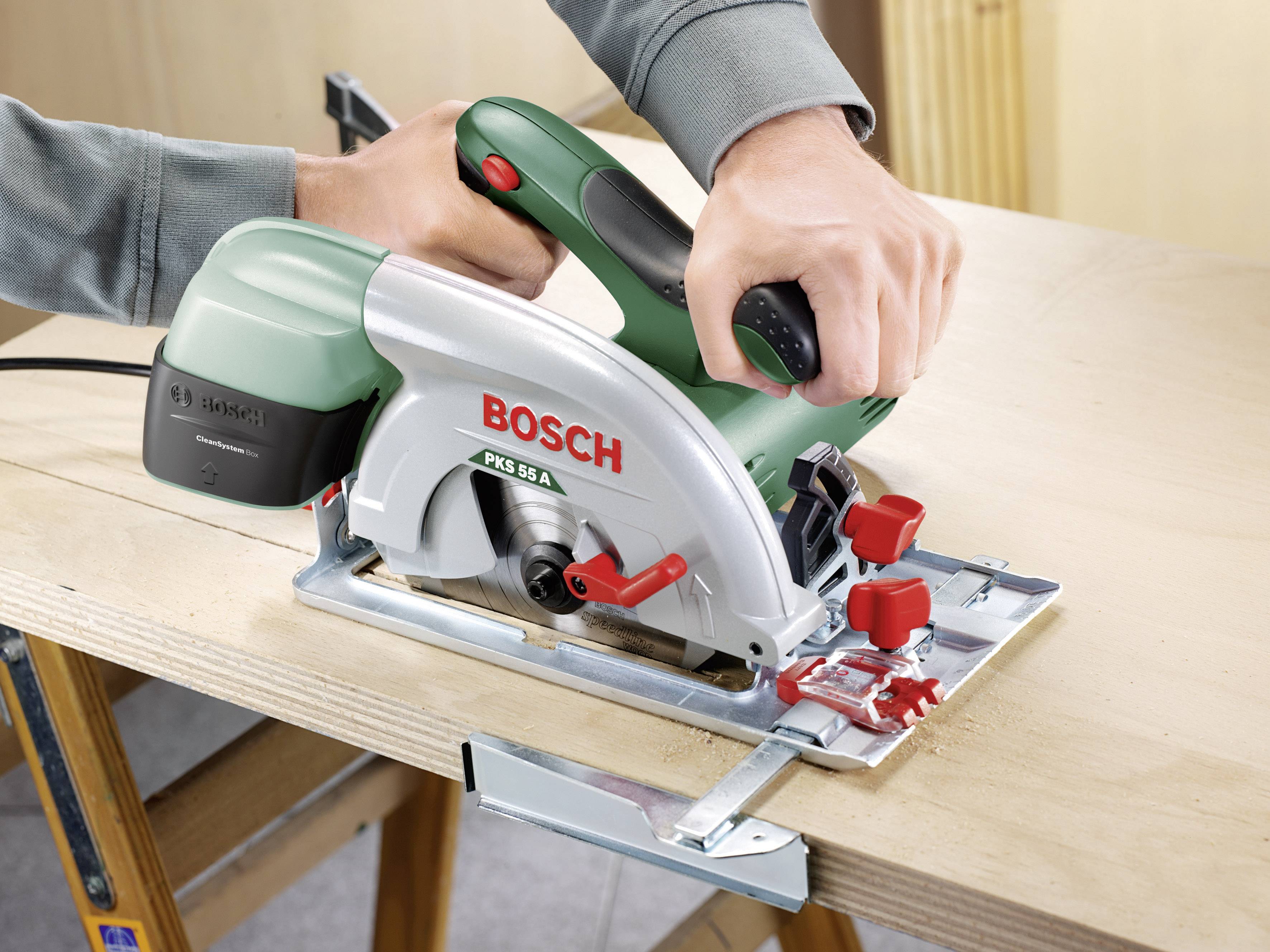 Una mano tiene una sega circolare verde e argentata del marchio Bosch, che sta tagliando un pannello di legno.