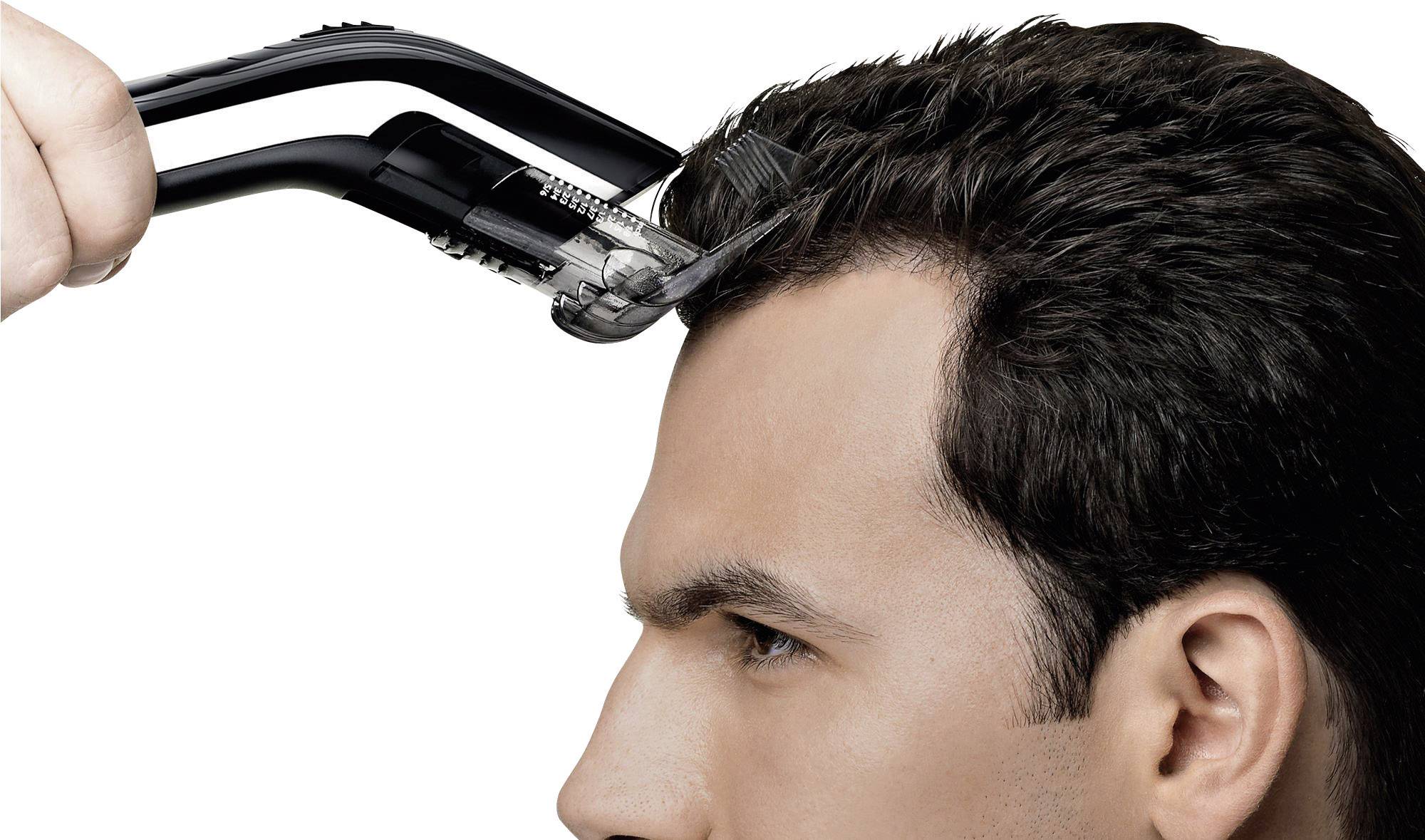 Un tagliapeli elettrico taglia i capelli di un uomo. L'uomo ha i capelli marroni, e lo sfondo è bianco.