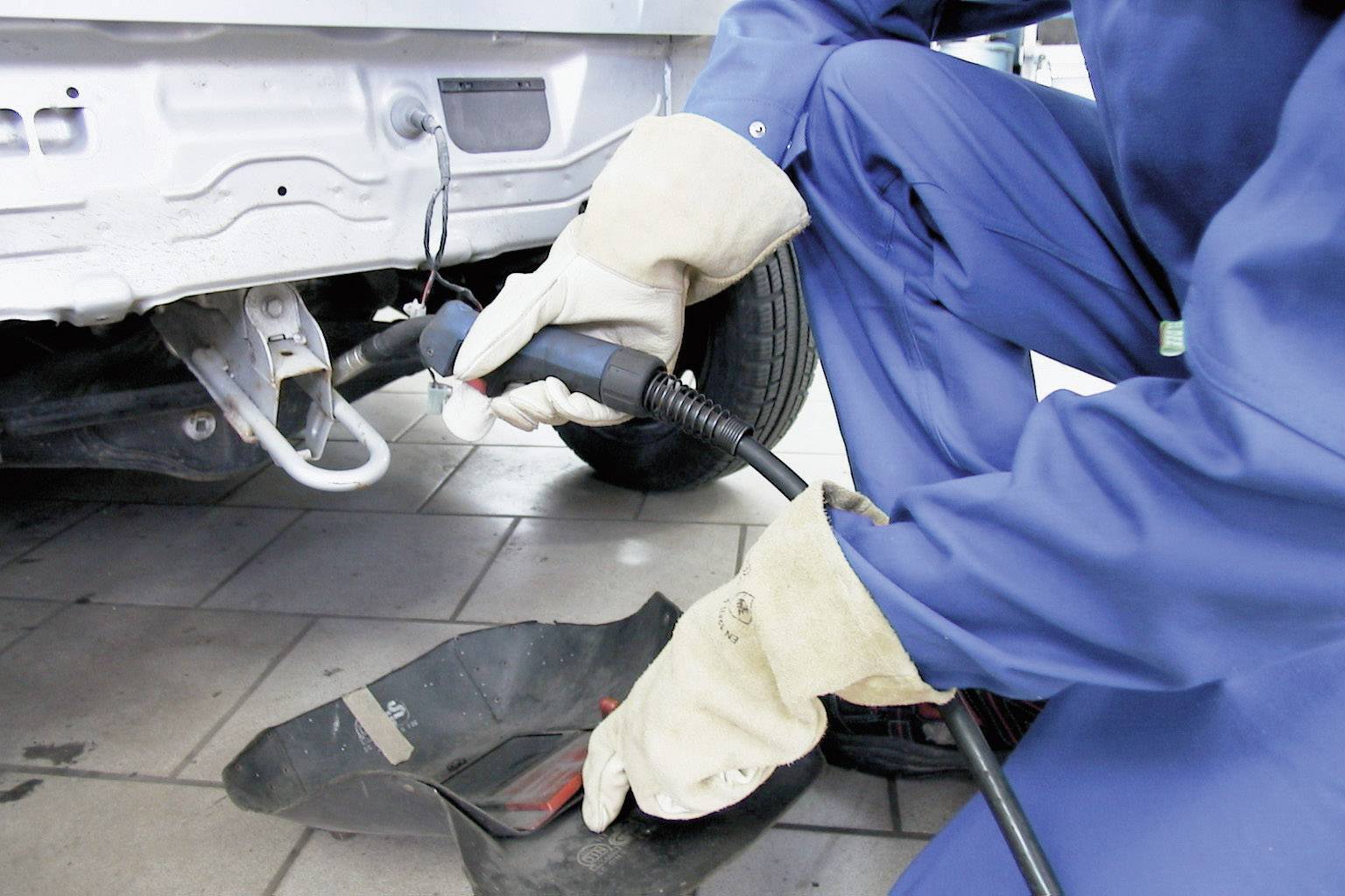 Un meccanico in tuta da lavoro blu sta saldando un telaio di un'auto in un'officina. I guanti lo proteggono dalle scintille.