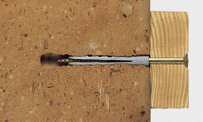 Un tassello è ancorato in un mattone per sostenere un pezzo di legno soprastante. Mostra il principio di ancoraggio.