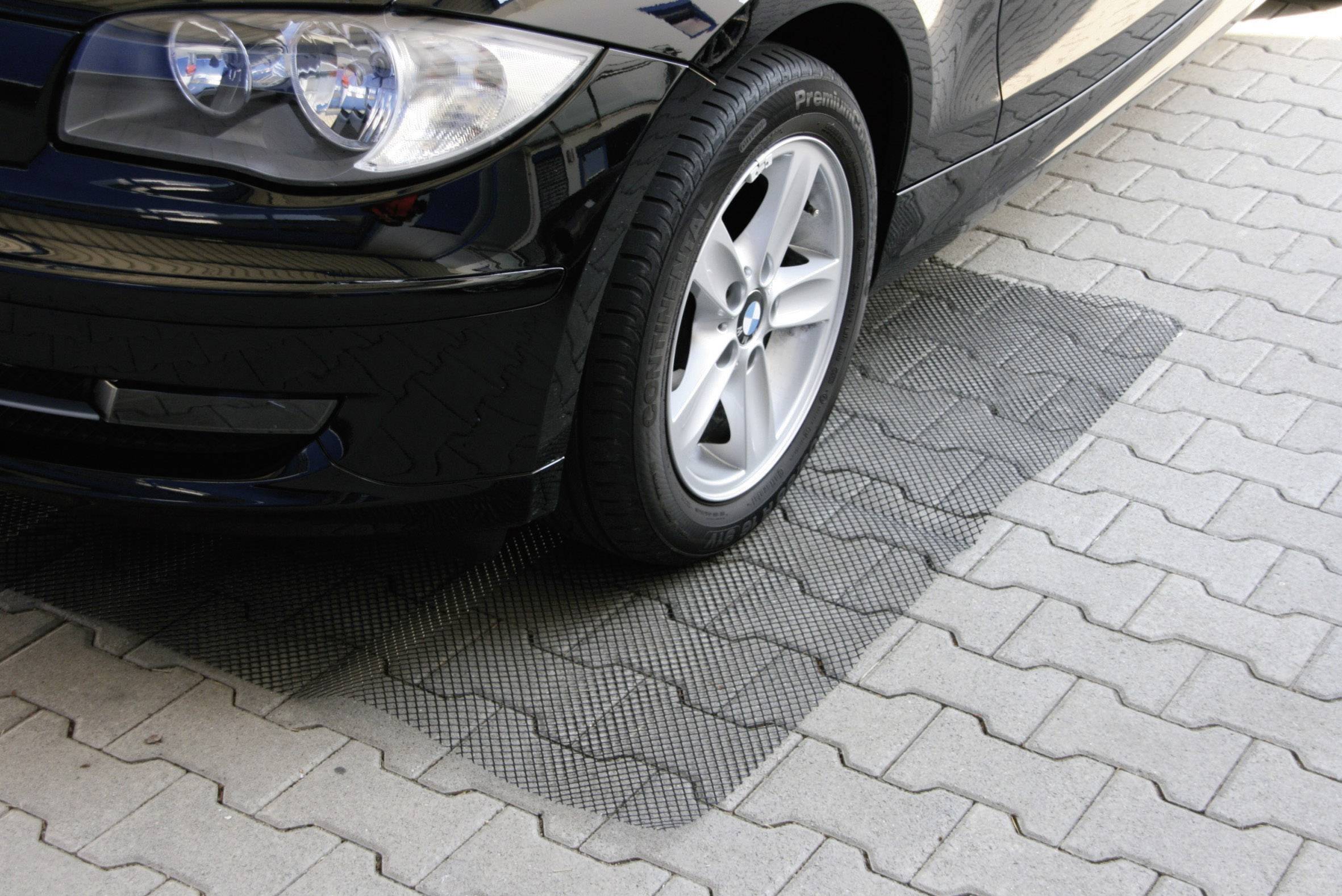 Un'auto nera è parcheggiata in uno spazio lastricato. La ruota anteriore destra è parzialmente poggiata su un tappetino gommato strutturato.