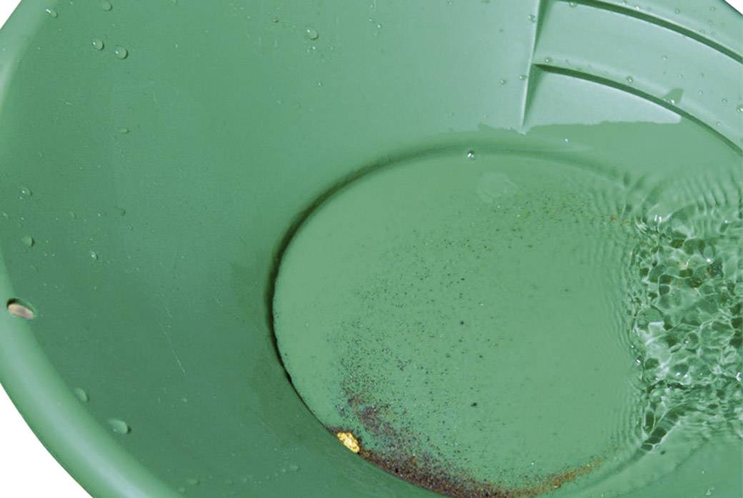 Una padella verde per la ricerca dell'oro, riempita di acqua con alcuni piccoli frammenti d'oro sul fondo.