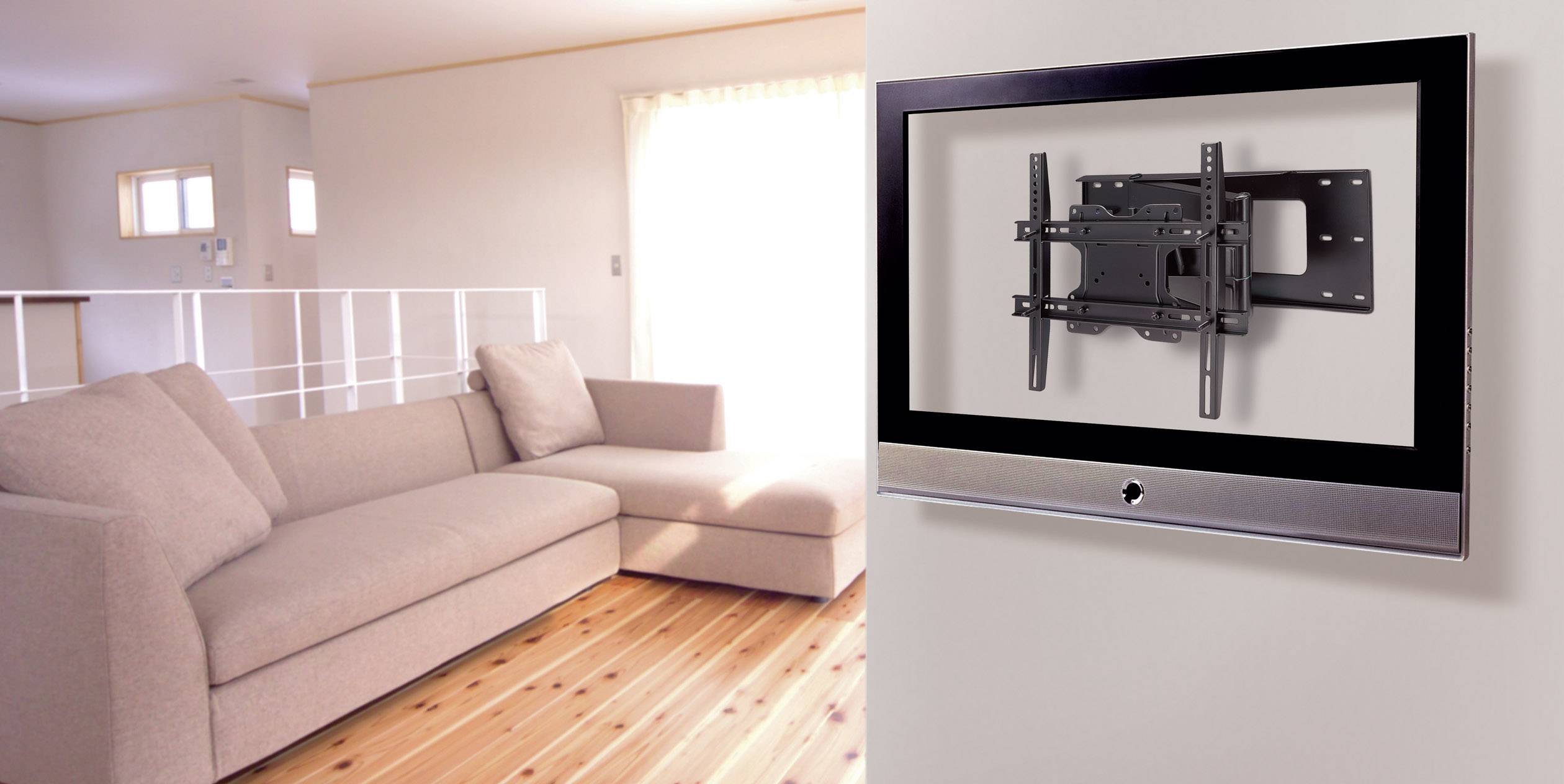 Un soggiorno moderno con un divano beige su un pavimento in legno. Sulla parete un supporto per TV senza televisore. Luce diurna luminosa proveniente da una finestra.