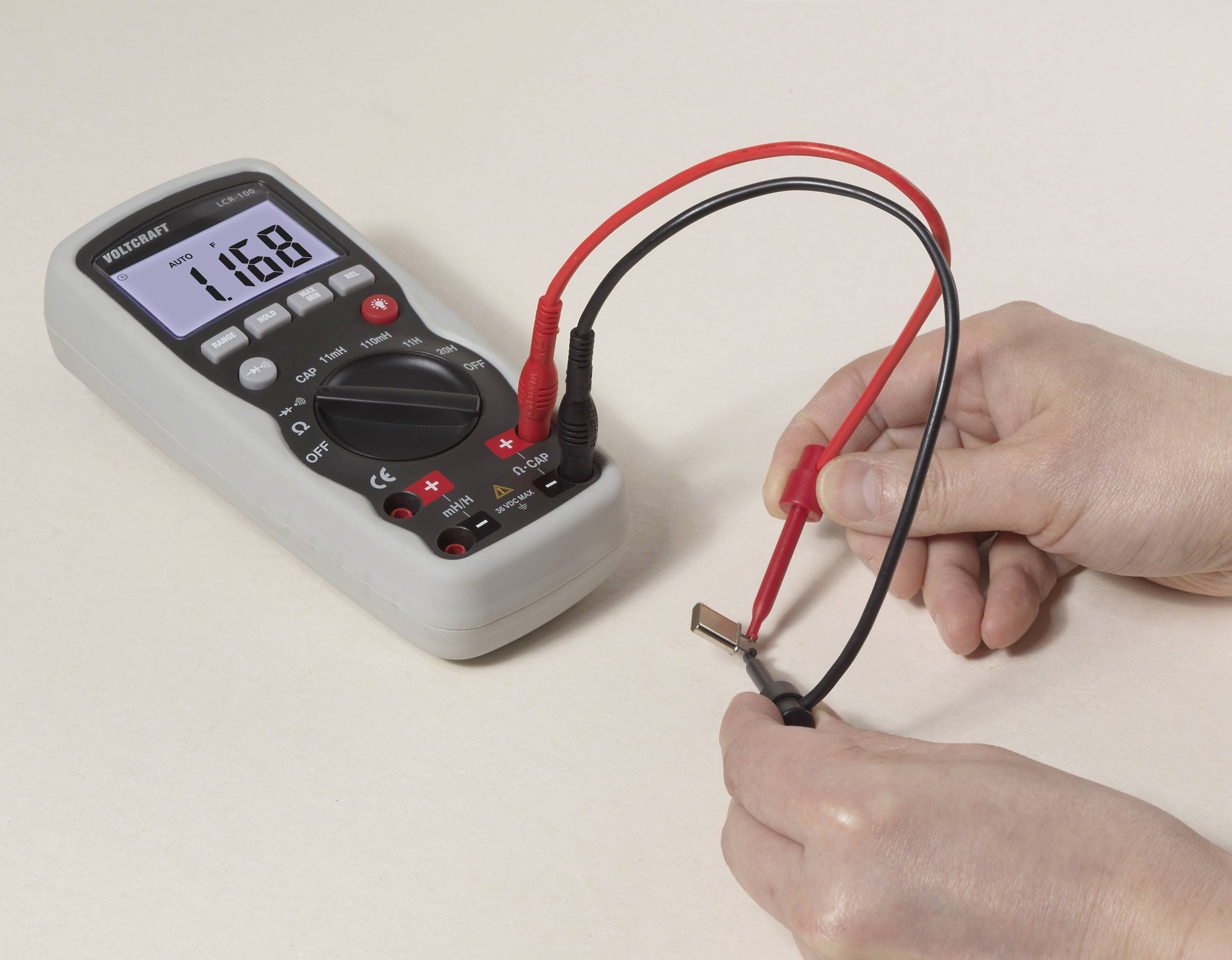 Een multimeter toont de waarde '11.68'. Een hand houdt de meetpennen tegen een kleine elektrische component.