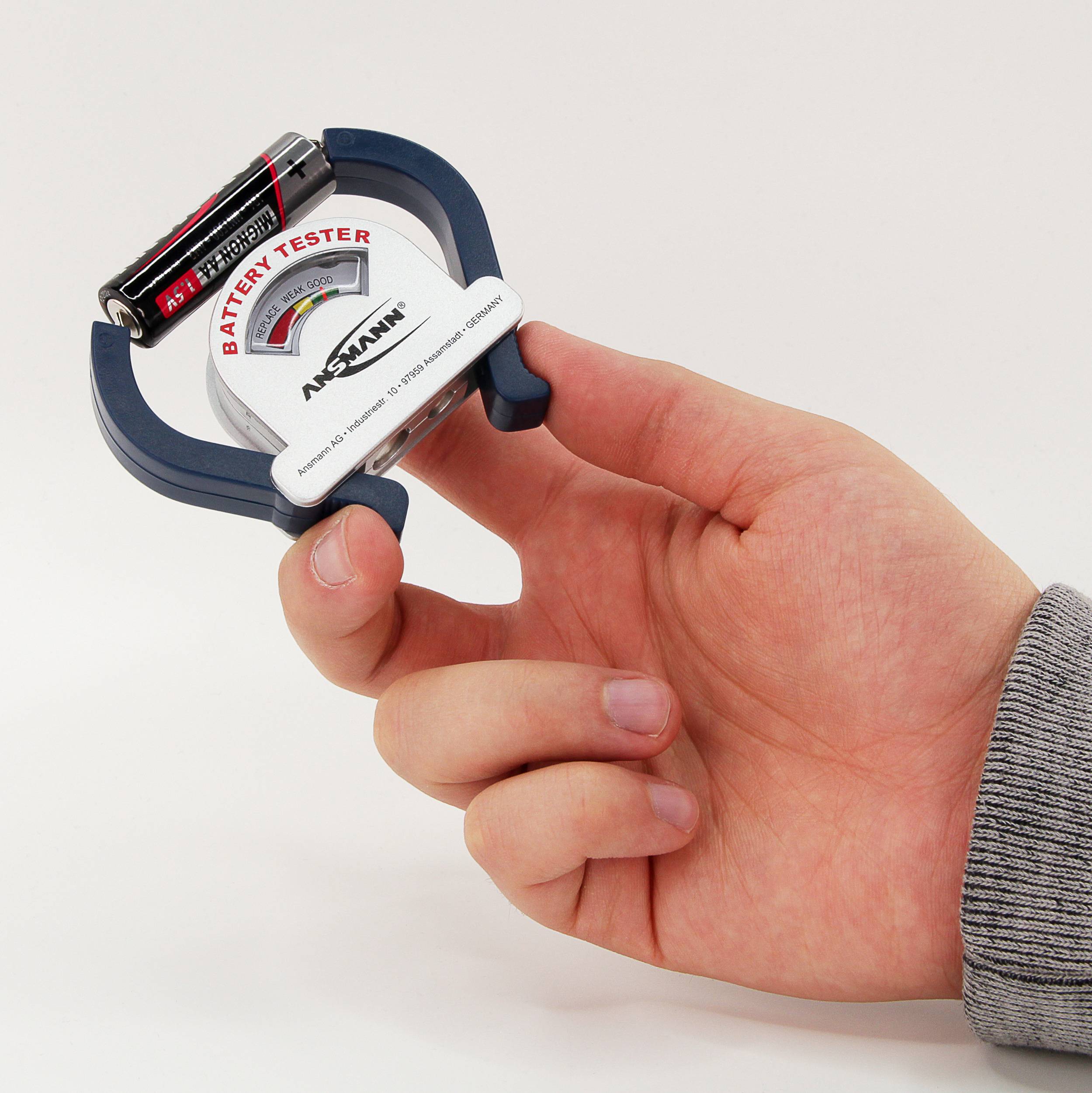 Een hand houdt een batterij-tester vast met een AA-batterij erin. De tester geeft de batterijstatus weer met een kleurendiagram.
