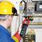 Een persoon in veiligheidsuitrusting controleert elektrische componenten met een multimeter in een schakelkast.