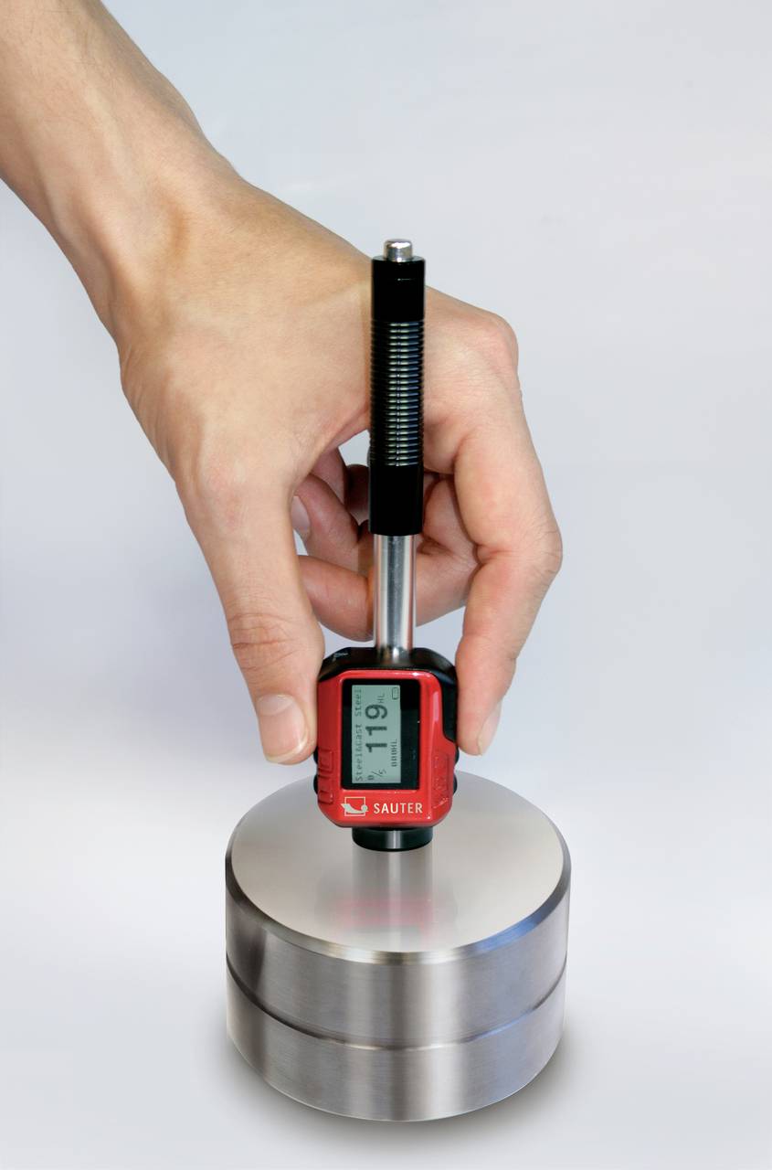 Een hand houdt een digitaal meetinstrument vast op een metalen cilinder, waarbij het display '119' toont.