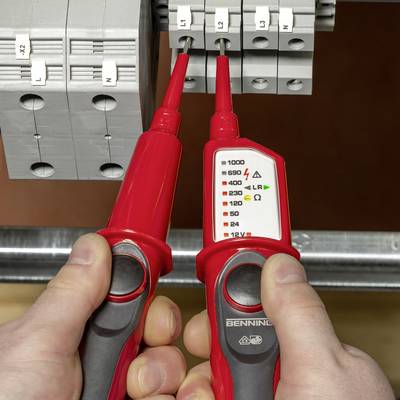 Een persoon houdt twee rode spanningstesters voor een grijze zekeringkast om elektrische spanning te meten.