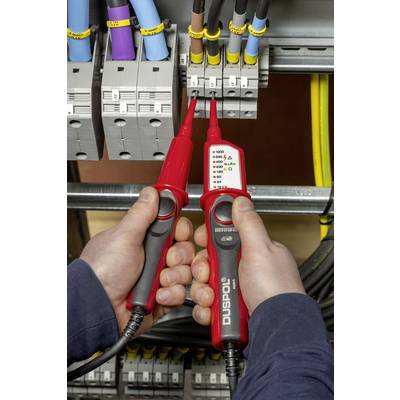 Twee handen houden een spanningszoeker vast om elektrische stroom te controleren in een schakelkast. Meerdere kabels zijn aangesloten.
