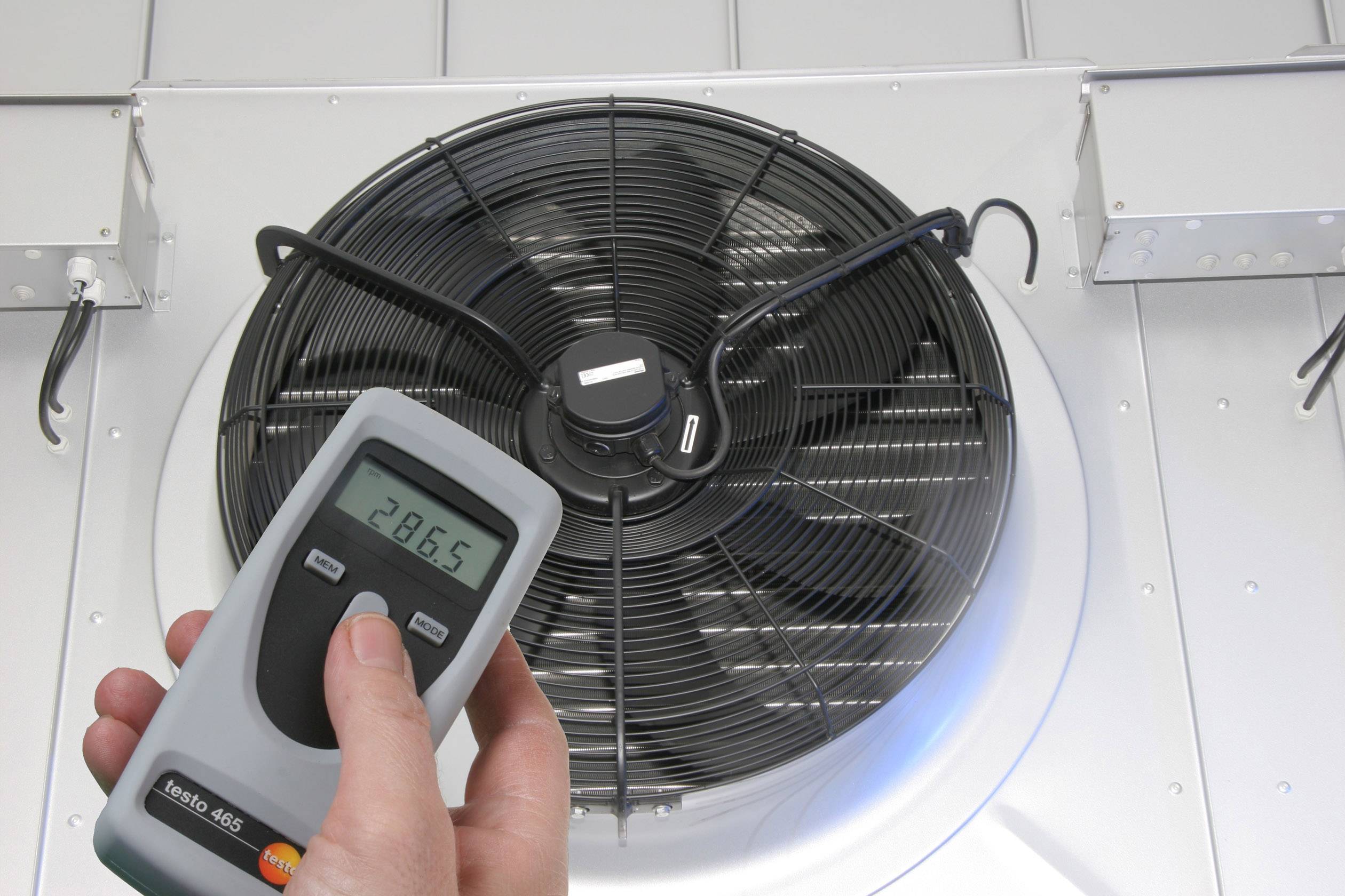 Een handapparaat toont '28,65', vastgehouden voor een grote ventilator in een ventilatiesysteem. Indicator voor temperatuur/klimaatregeling.