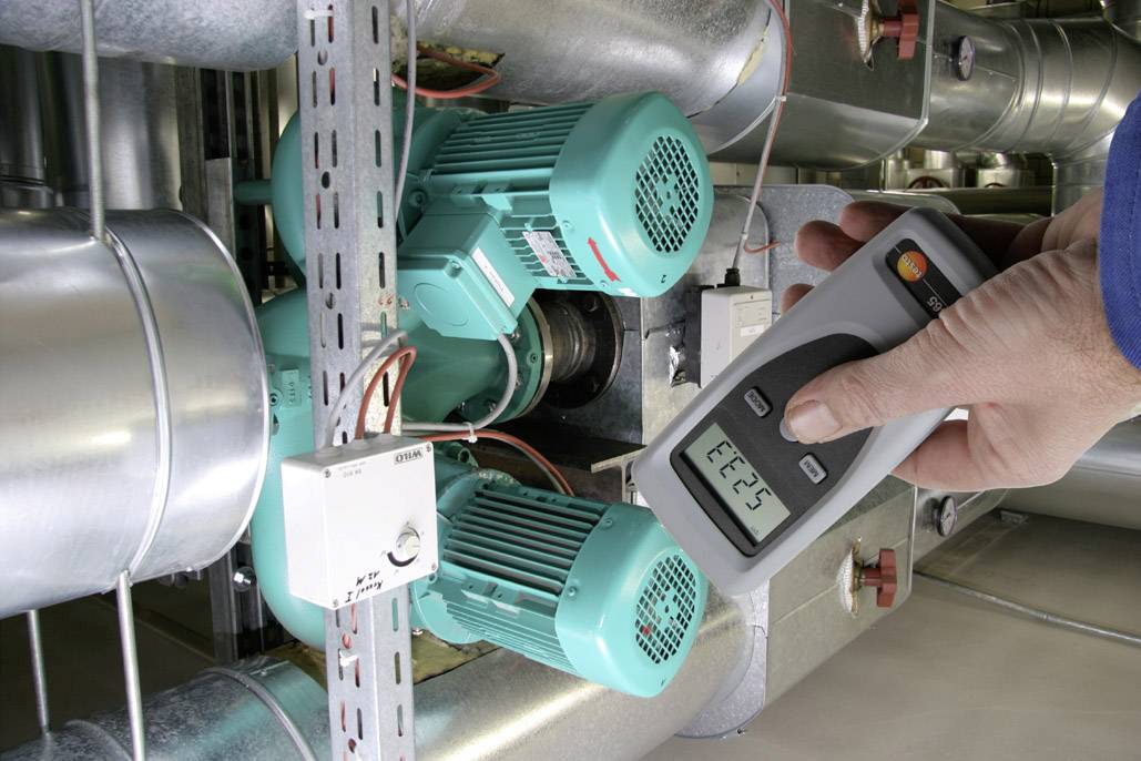 Een persoon meet met een digitaal apparaat het elektrisch vermogen van twee groene motoren in een industriële installatie.