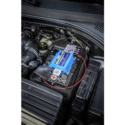 Autoaccu in de motorruimte met een blauw elektronisch apparaat erop. Het apparaat is verbonden met een rood kabel.