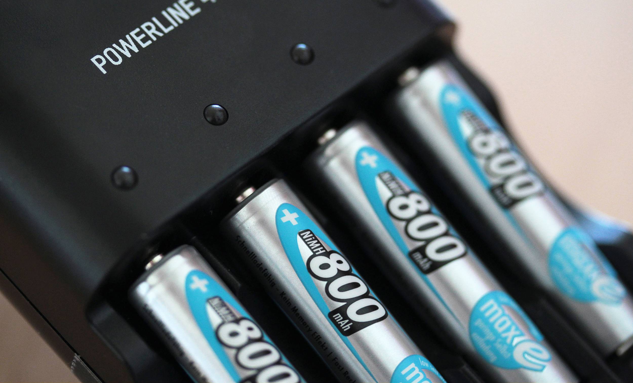 Een batterijlader laadt vier oplaadbare AA-batterijen met blauwe en zilveren etiketten. Bovenaan staat 'POWERLINE 4 LIGHTS'.