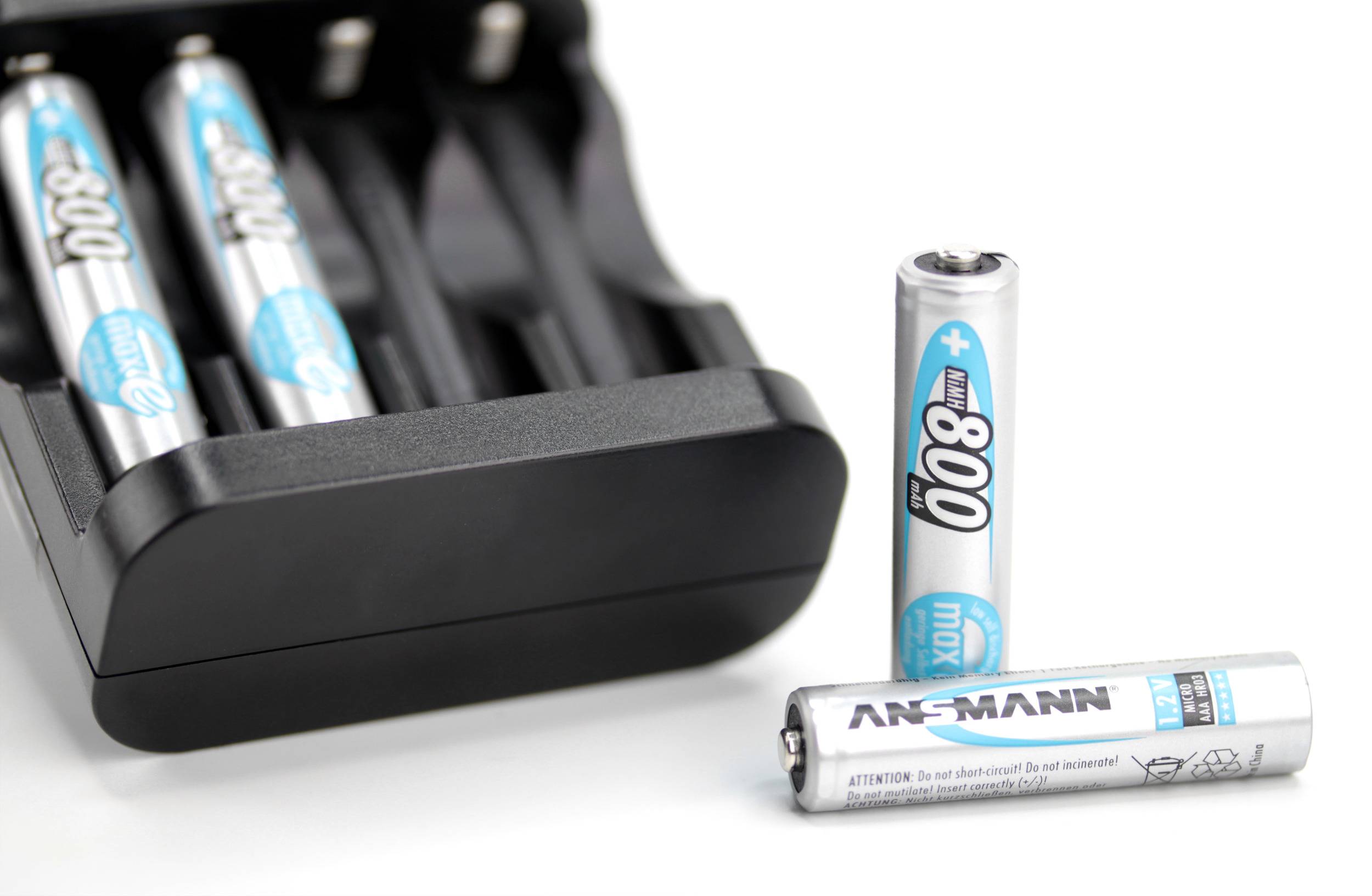 Een batterijlader is gedeeltelijk gevuld met blauw-witte AA-batterijen; er ligt nog een batterij voor de lader.