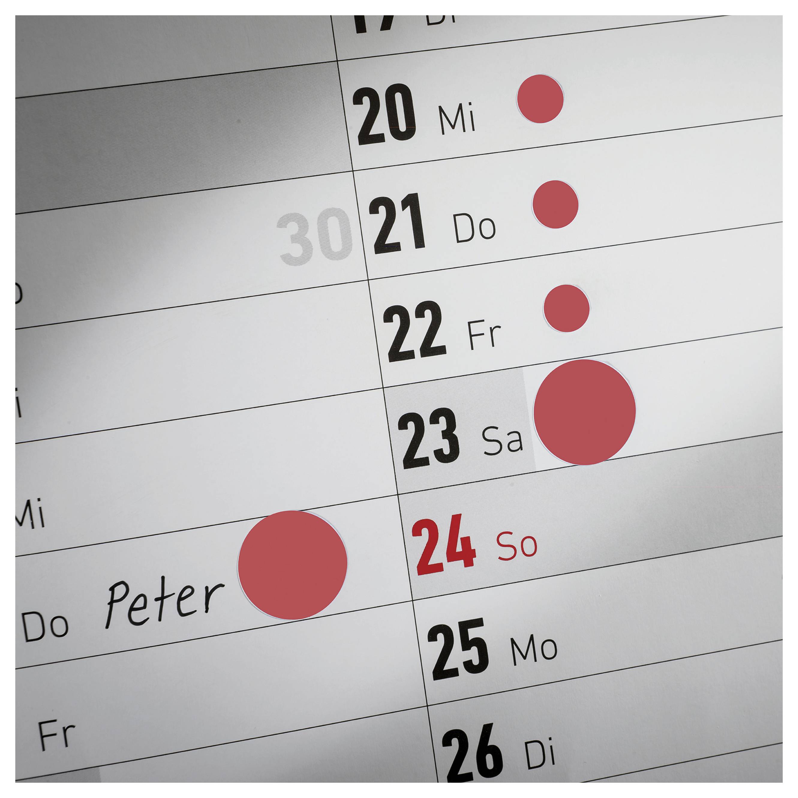 Closeup van een kalender met de dagen 20 tot 26; rode puntjes markeren afspraken, op 23 za een groot punt en op 24 zo een ingeschreven naam 'Peter'.