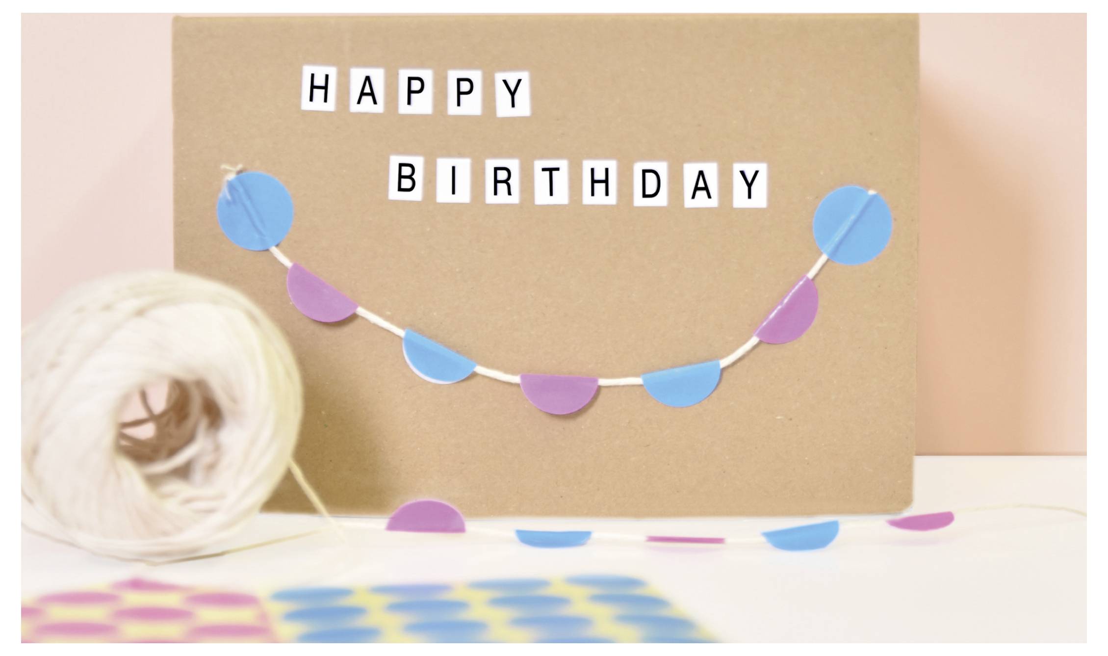 Verjaardagskaart met de opschrift 'HAPPY BIRTHDAY', kleurig versierd met een slinger en confetti, ernaast een touwtje.