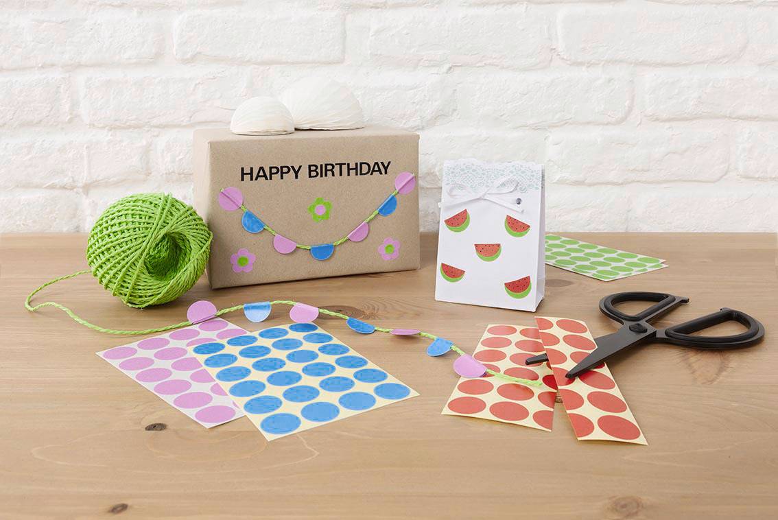 Geschenkdoos met 'Gefeliciteerd met je verjaardag'-opdruk, versierd met kleurrijke papieren slingers, omringd door knutselbenodigdheden zoals stickers, schaar en garen.