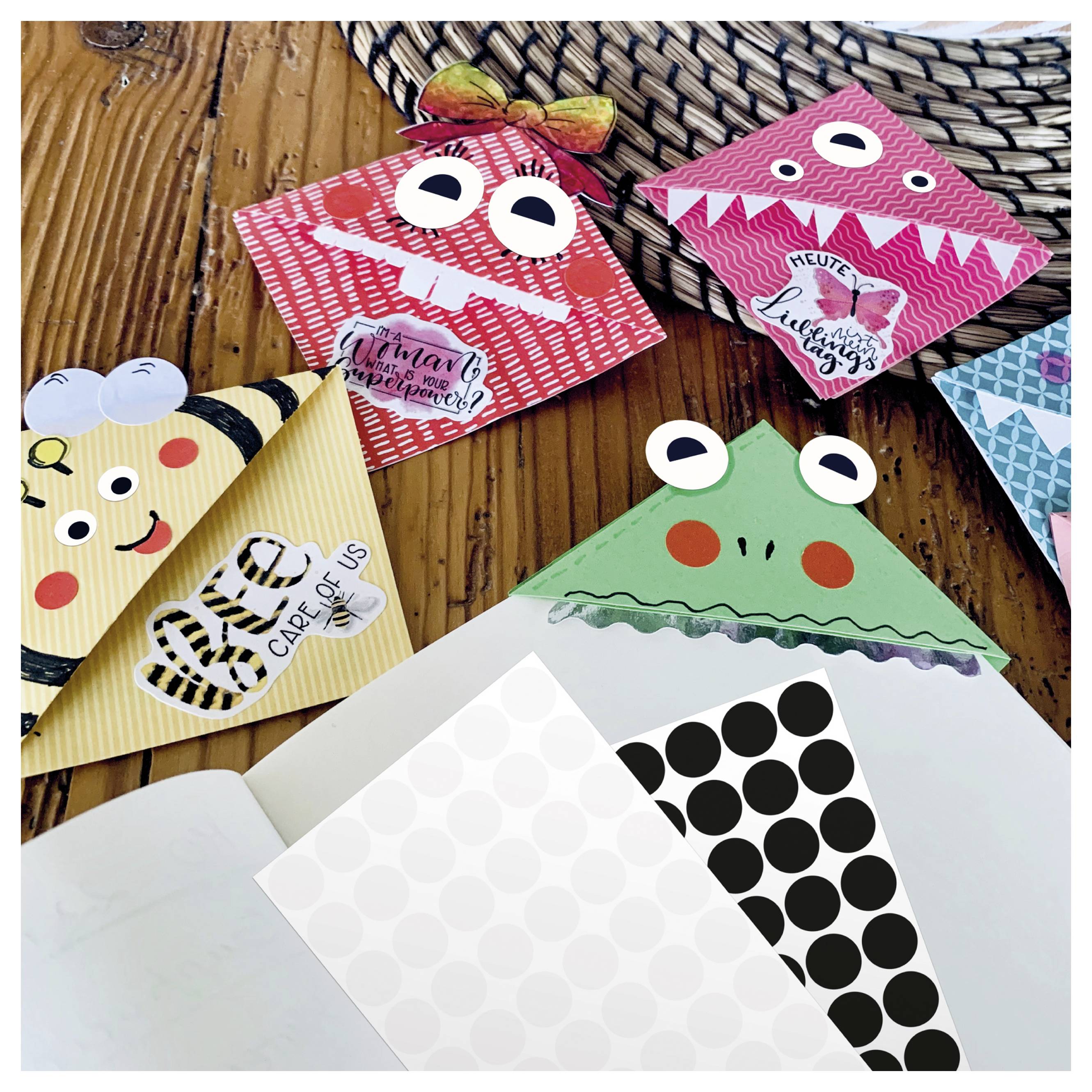 Meerdere gekleurde origami-boekenleggers met dierengezichten liggen op een houten tafel; op de voorgrond zijn geopende enveloppen en gestippelde papierbladen zichtbaar.