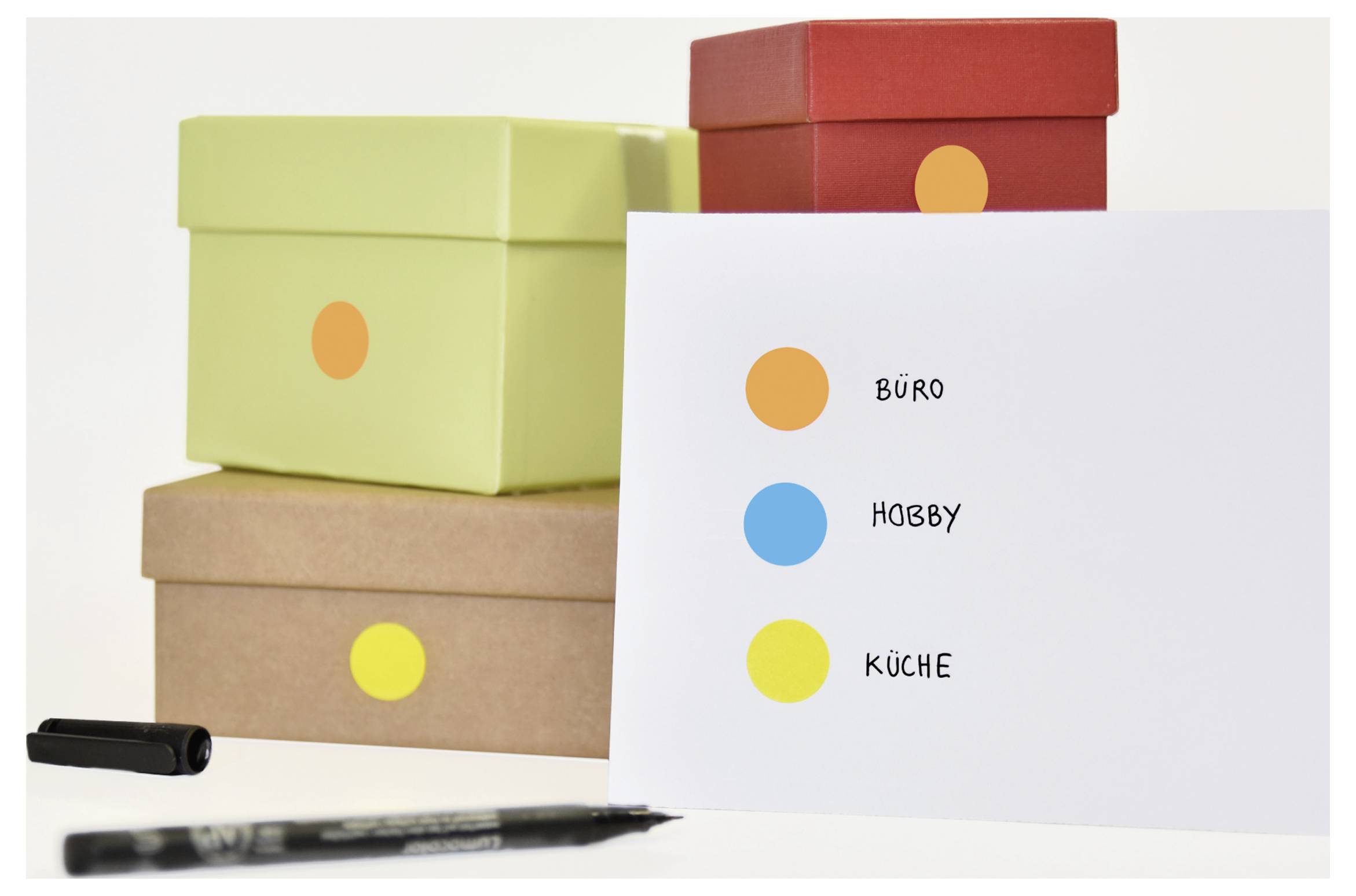 Gelabelde opslagdozen met gekleurde stippen en lijst: 'KANTOOR', 'HOBBY', 'KEUKEN'; toont een indeling naar categorieën.
