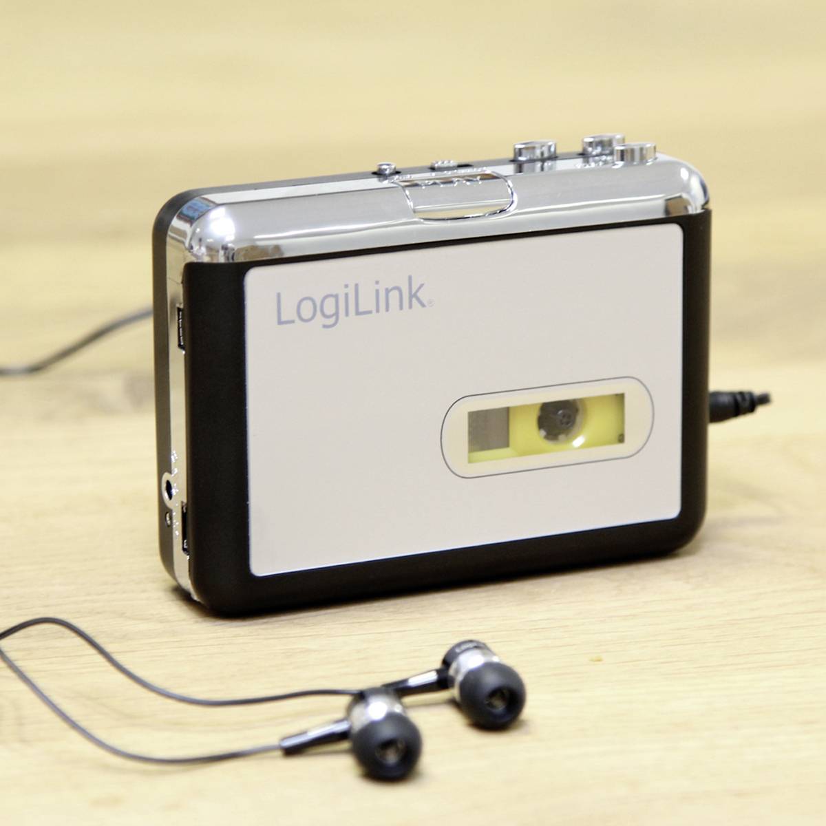Een zilveren cassetterecorder met zwarte details en logo 'LogiLink', op een houten tafel. Ernaast liggen zwarte oordopjes.