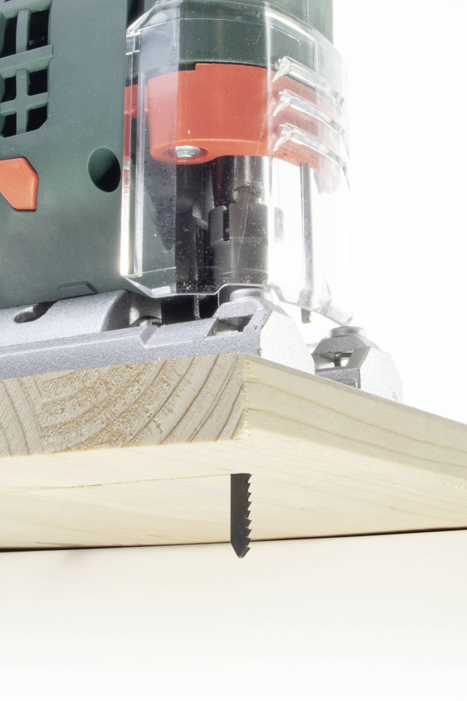 Een groene decoupeerzaag met een rood detail zaagt hout onder een schuine hoek. Het zaagblad is gedeeltelijk zichtbaar onder het werkstuk.