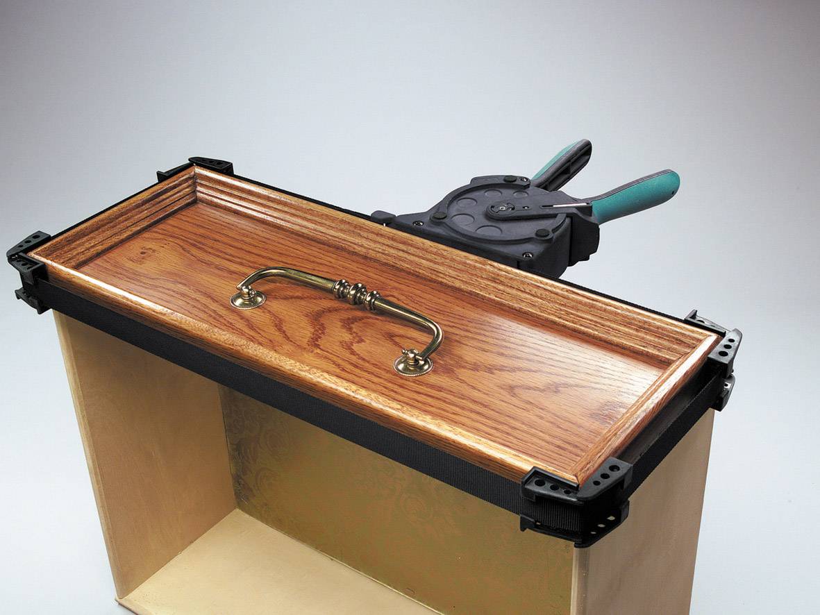 Houten kist met open deksel en metalen handvat; een tang met groene greep ligt ernaast.