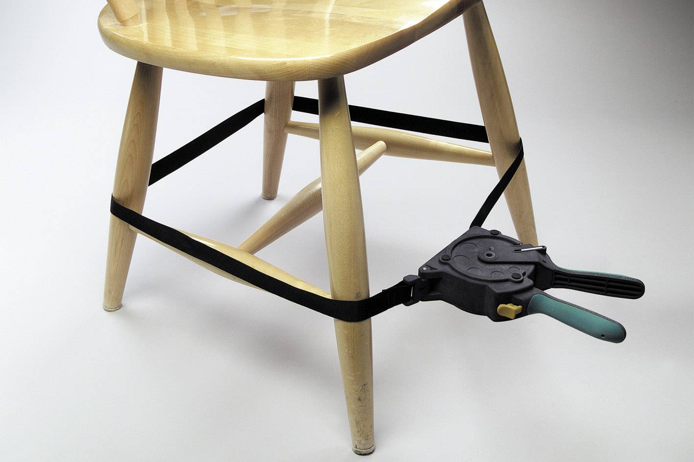 Een houten stoel waarvan de poten zijn vastgezet met een spanklem en een klem, staat op een lichte vloer.