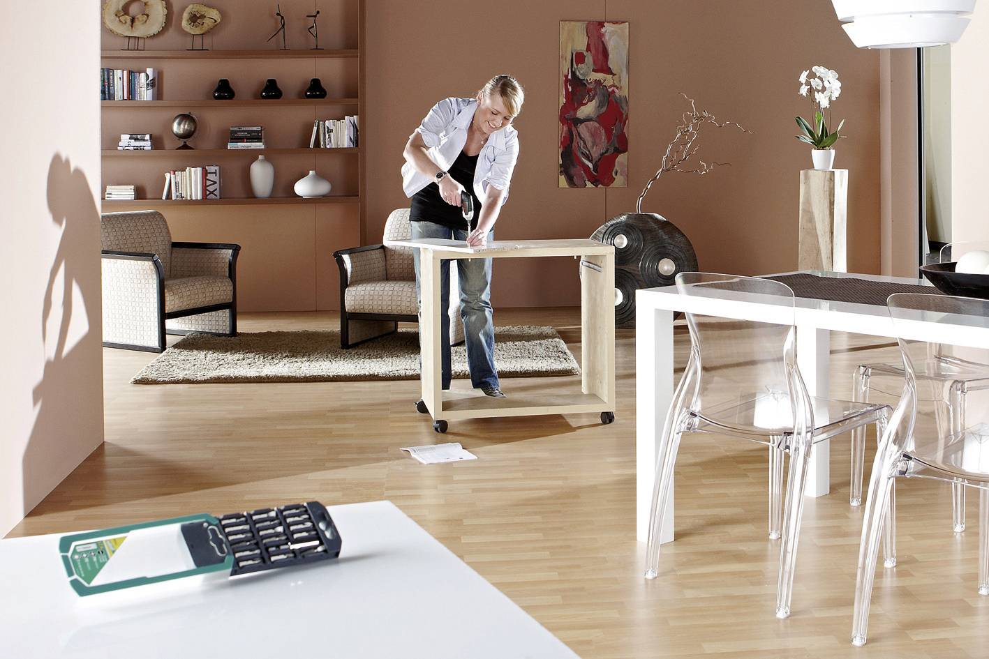 Een persoon strijkt een overhemd in een modern ingerichte ruimte met houten vloer, strijkplank en glazen tafel op de voorgrond.