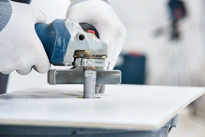 Een persoon slijpt een metalen rand met een slijpmachine. Hij draagt witte handschoenen om veiligheid te waarborgen.