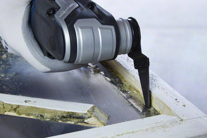 Een close-up van een multifunctioneel gereedschap dat nauwkeurige snedes maakt in een witte raamlijst om glas te verwijderen.