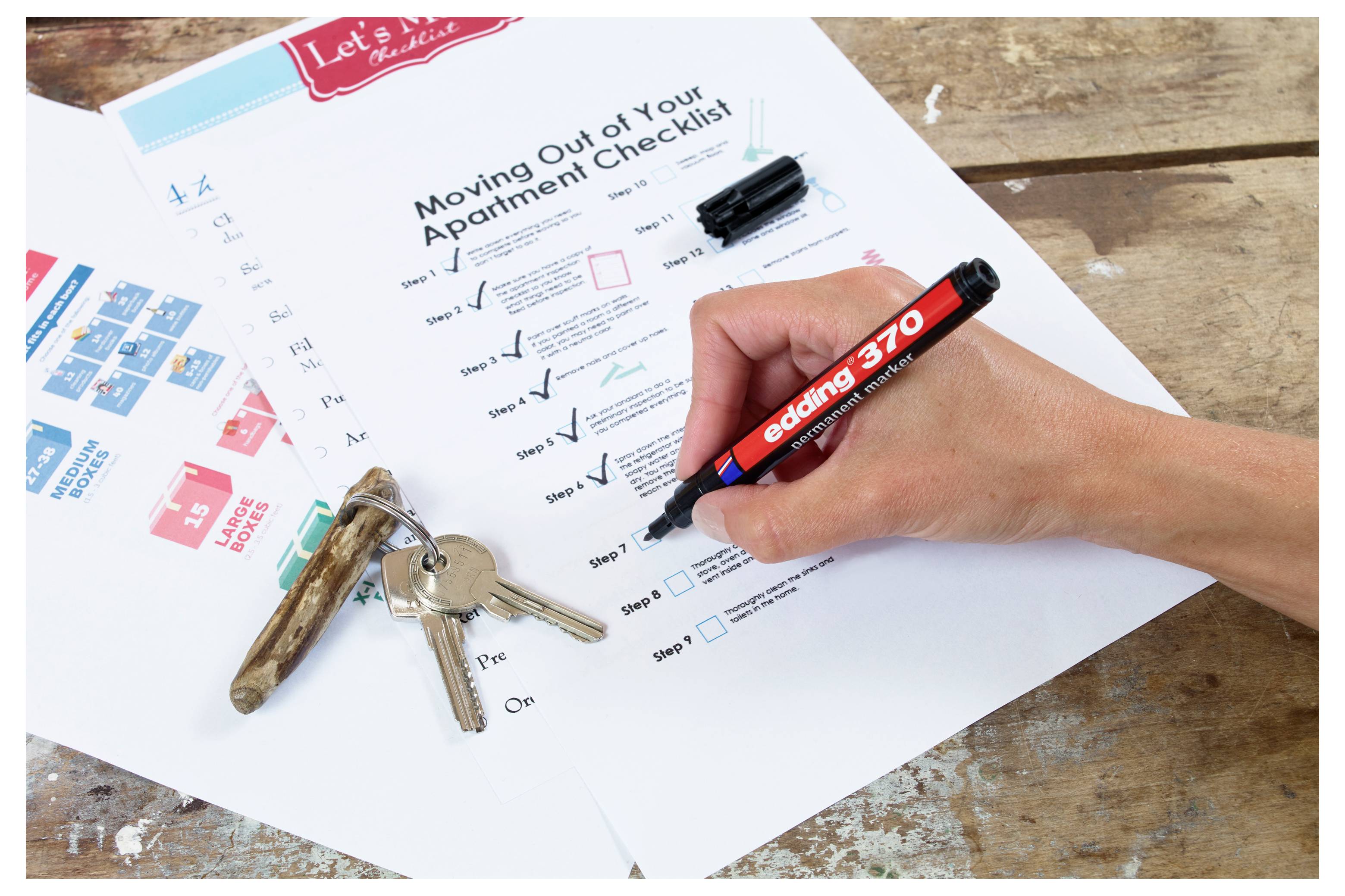 Hand die een verhuisappartementen checklist afvinkt met een oranje marker naast een stel huissleutels op een houten tafel.