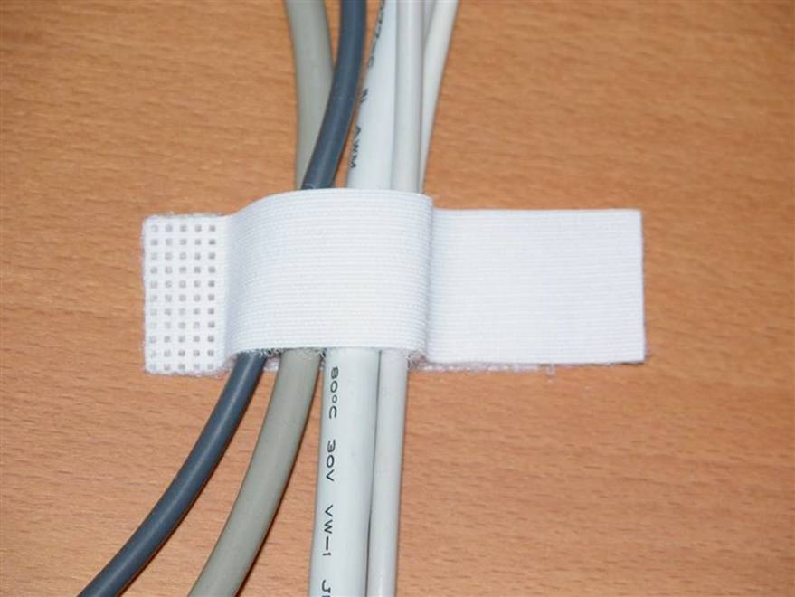 Meerdere kabels worden netjes bij elkaar gehouden met een wit klittenband op een houten tafel.