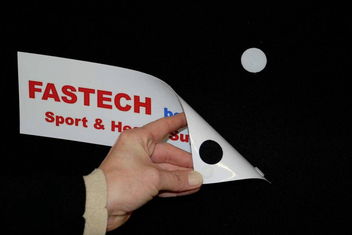 Een hand houdt een bord vast met de tekst 'FASTECH Sport & Home Solutions', dat met een klittenband bevestigd is aan een zwart oppervlak.