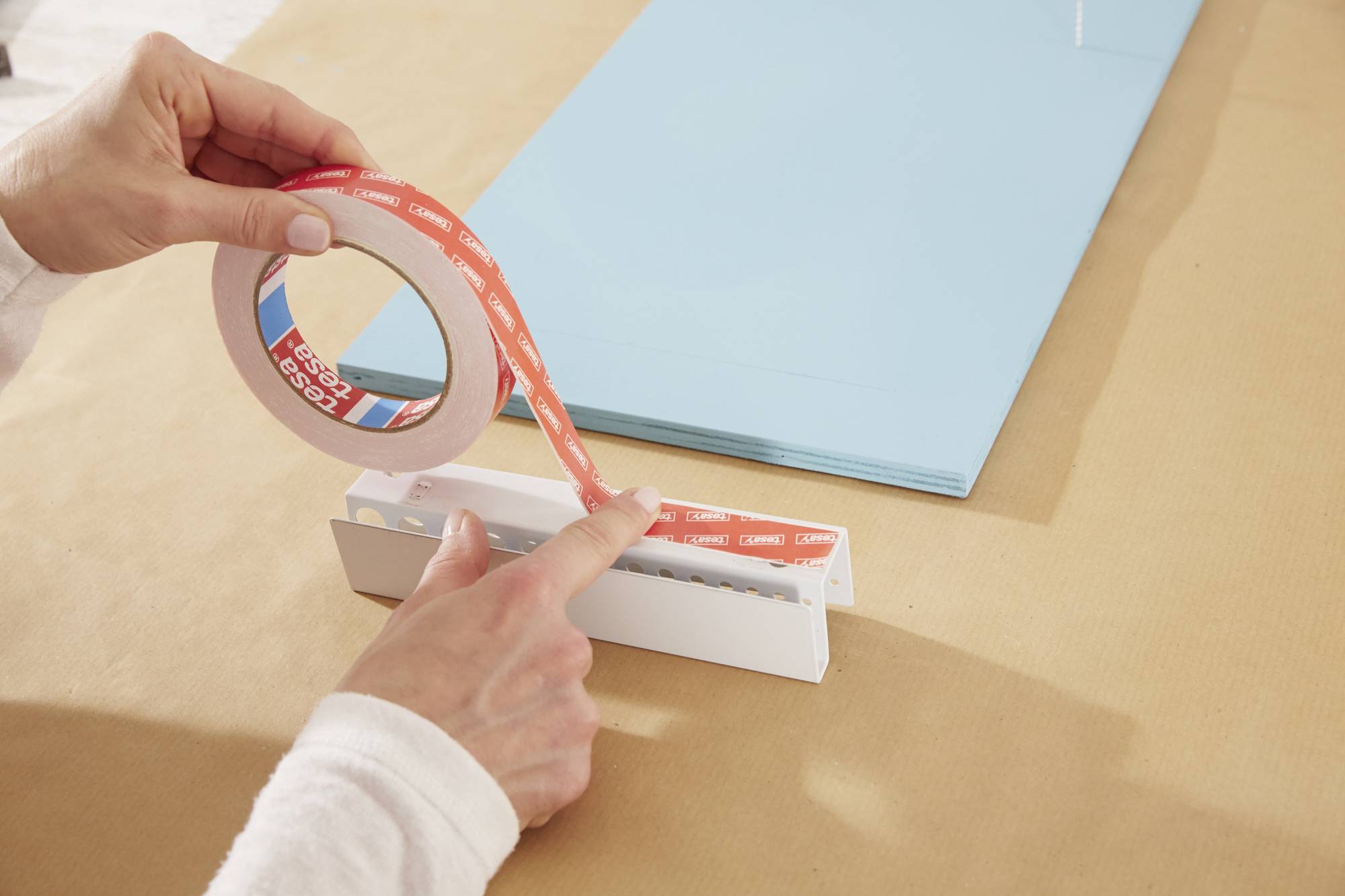 Een persoon bevestigt een dubbelzijdige plakband op een papierhouder, terwijl blauw papier ernaast ligt.
