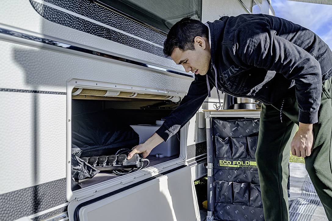 Een man bergt spullen op in een opbergruimte van een camper. Ernaast staat een mand met het opschrift 'Eco Fold'.