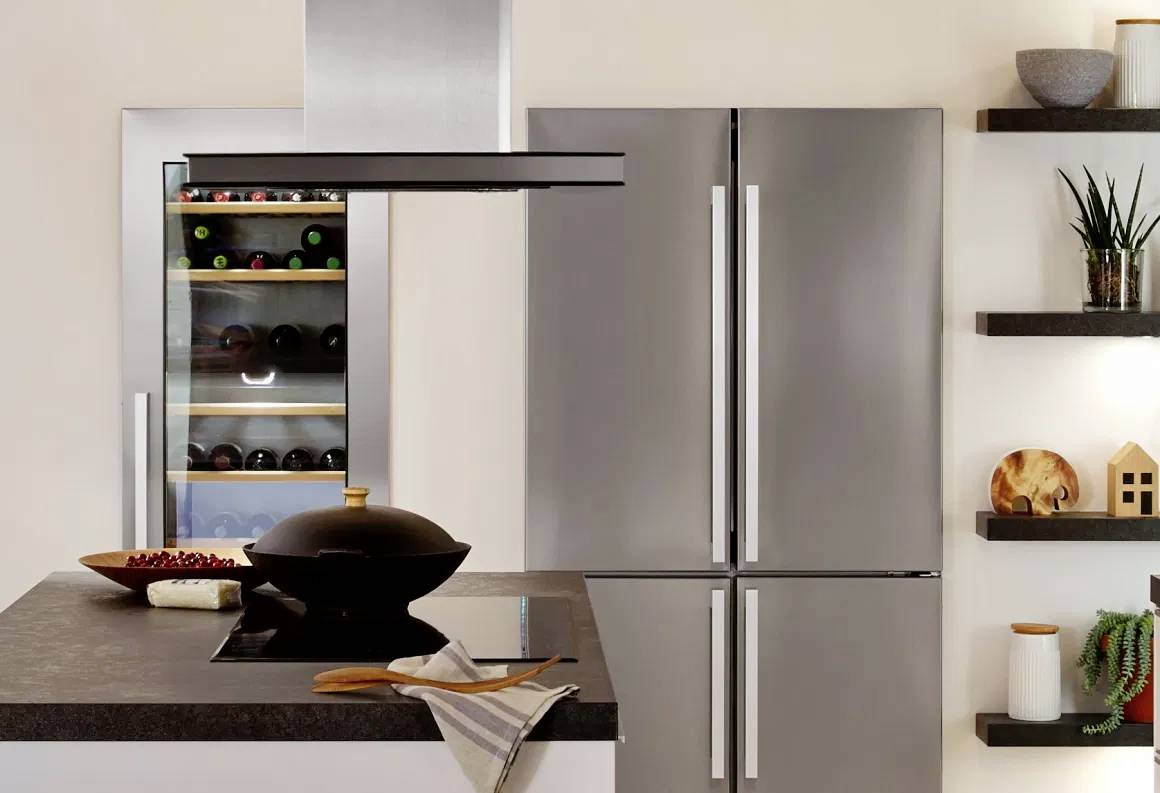 Moderne keuken met grijze koelkast, wijnkoeler, kookeiland en open schappen. Planten en decoraties zorgen voor gezelligheid.