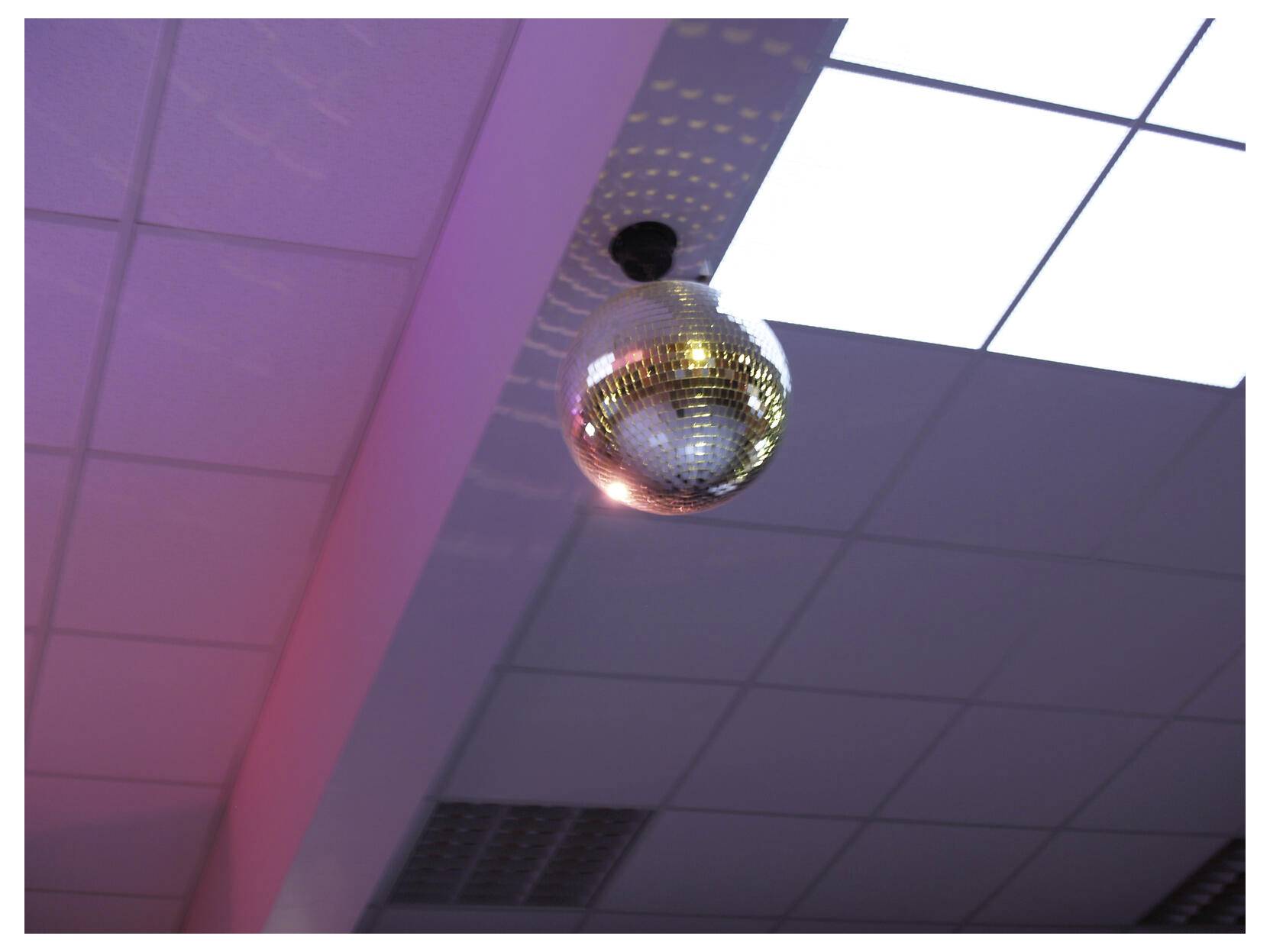 Een gespiegelde discobal hangt aan het plafond onder paars en wit licht.