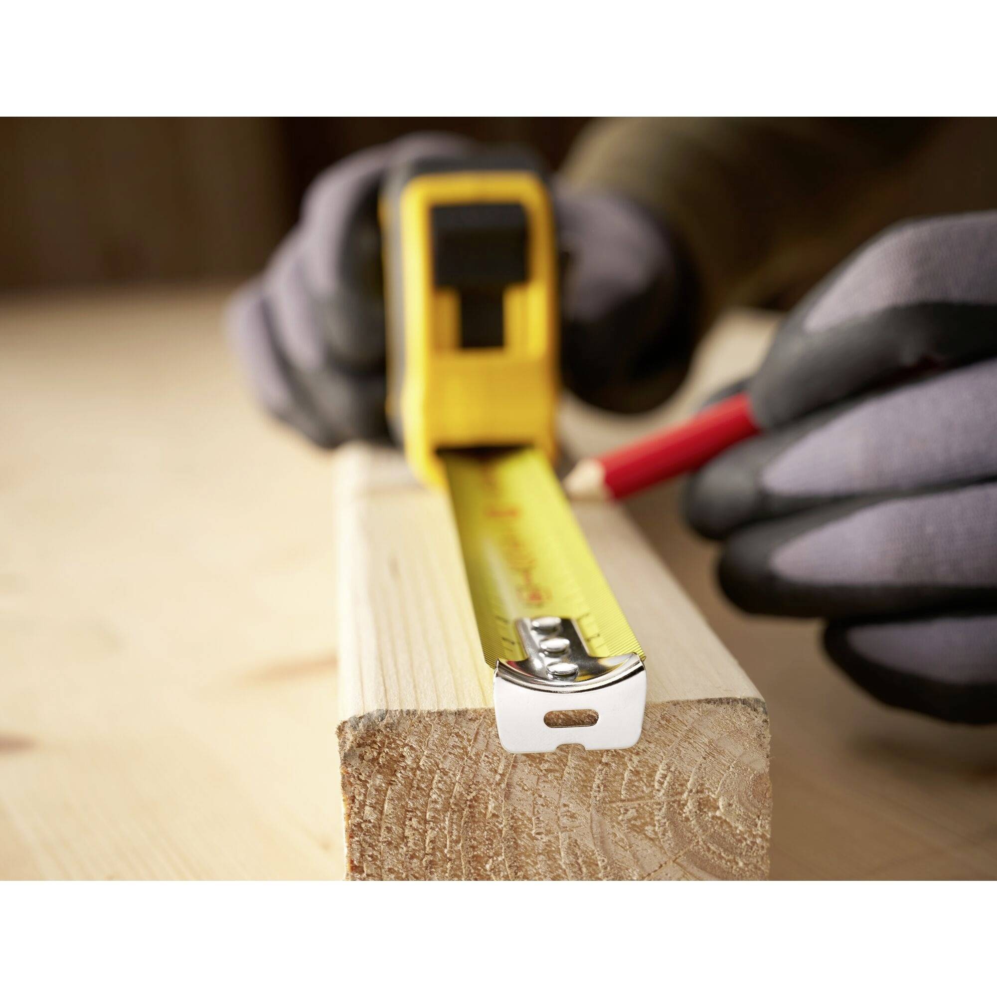 Een persoon markeert een houten plank met een rode pen en meet deze met een meetlint.