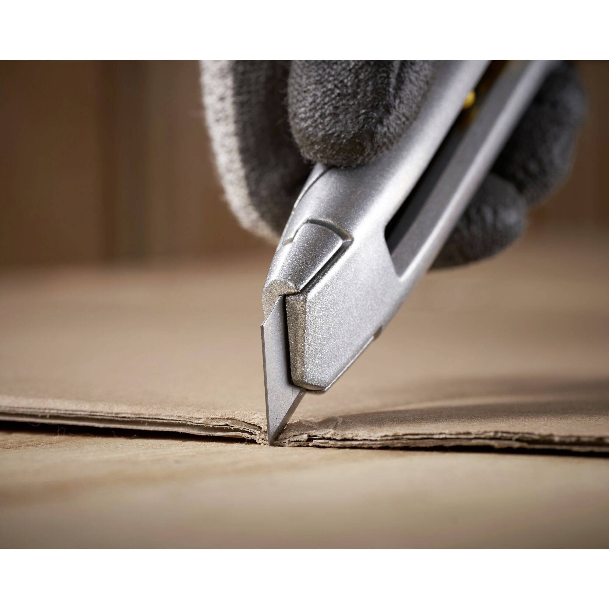 Een gehandschoende hand gebruikt een zilveren tapijtenmes om een doos nauwkeurig te snijden.