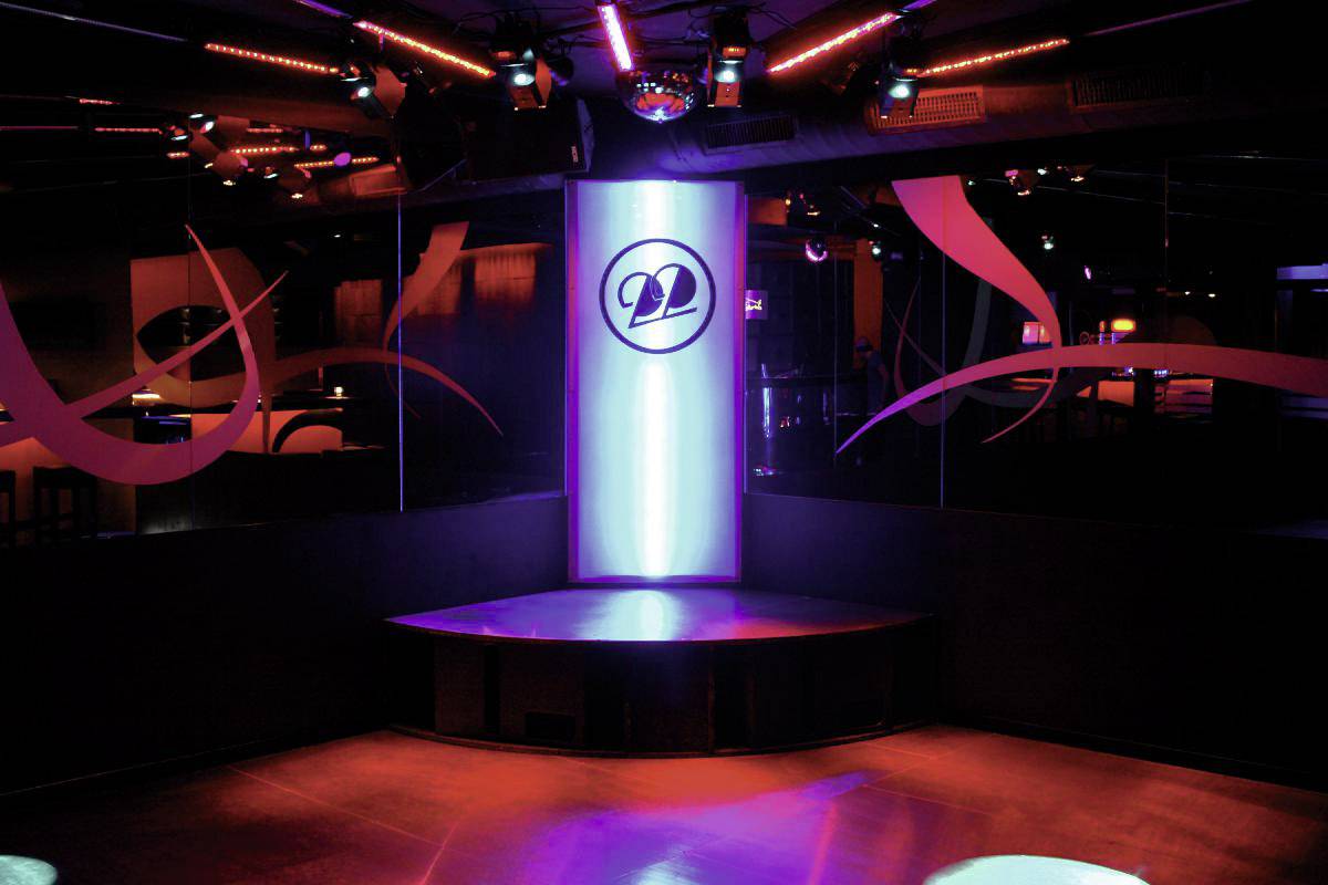 Een lege podium in een nachtclub, verlicht door kleurrijke lampen met een glanzende paal in het midden.