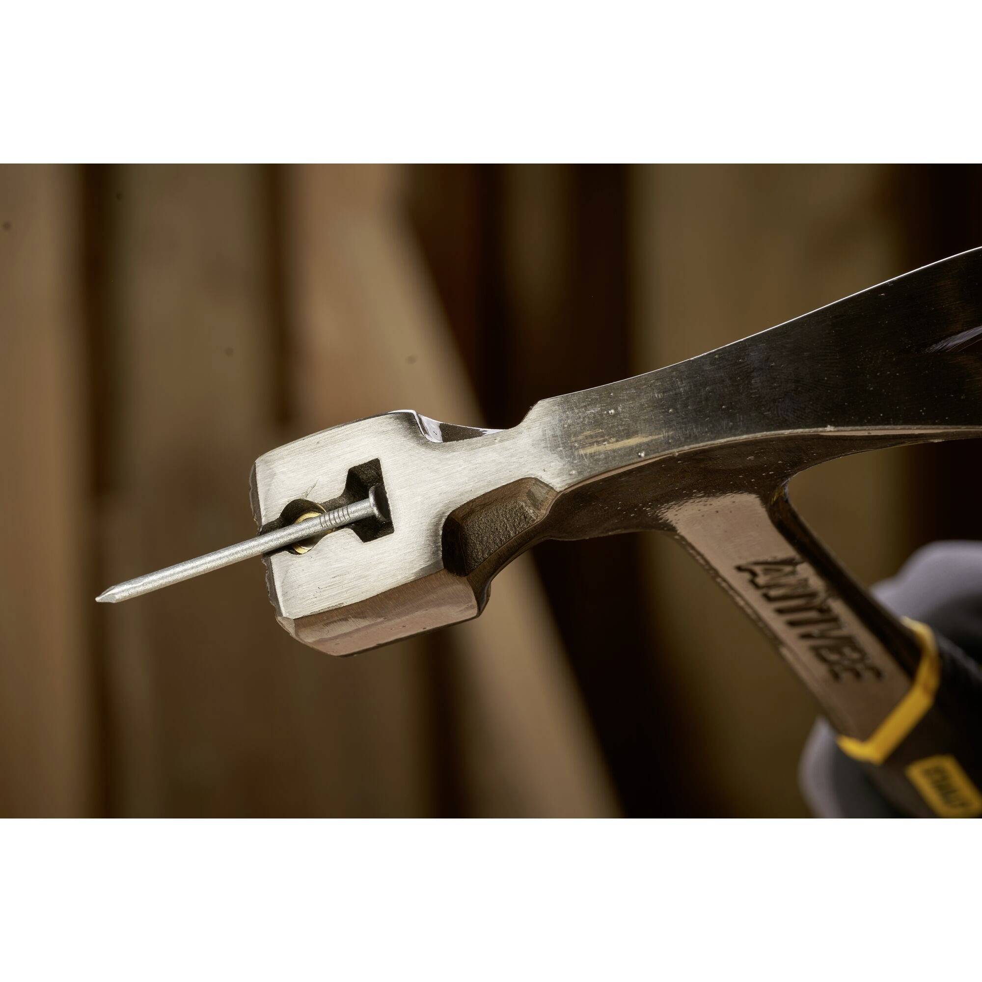 Een hamer tilt een houten spijker, toont een close-up met focus op het gereedschap en de kop van de spijker in de tang.