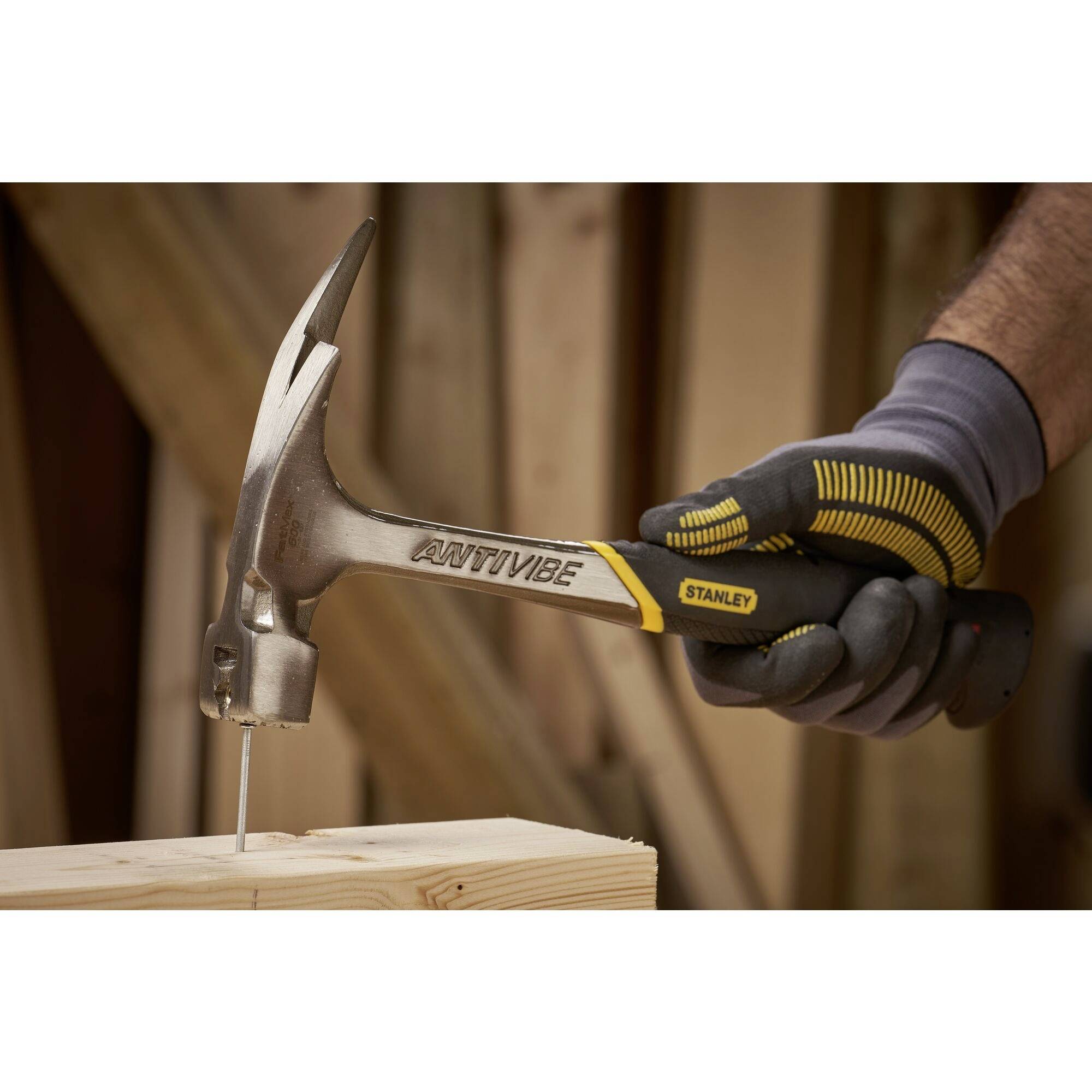 Een hand met handschoen houdt een hamer vast en slaat een spijker in een stuk hout.