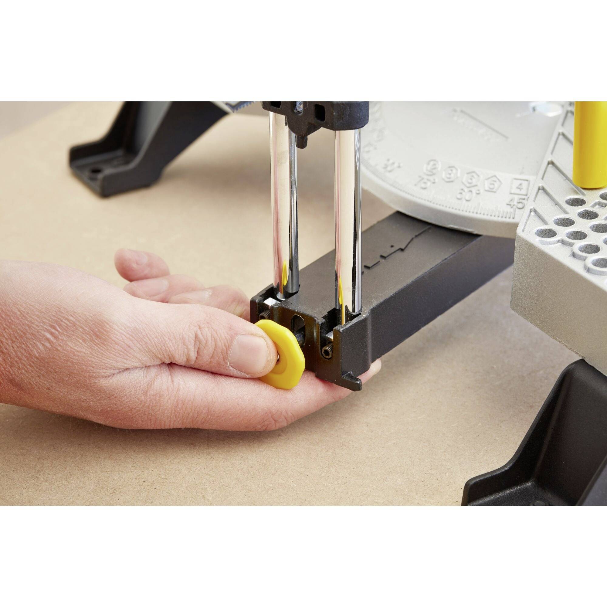 'Een hand drukt op een gele knop aan een metalen toestel dat op een tafel is bevestigd. De focus ligt op de staven en de handbeweging.'